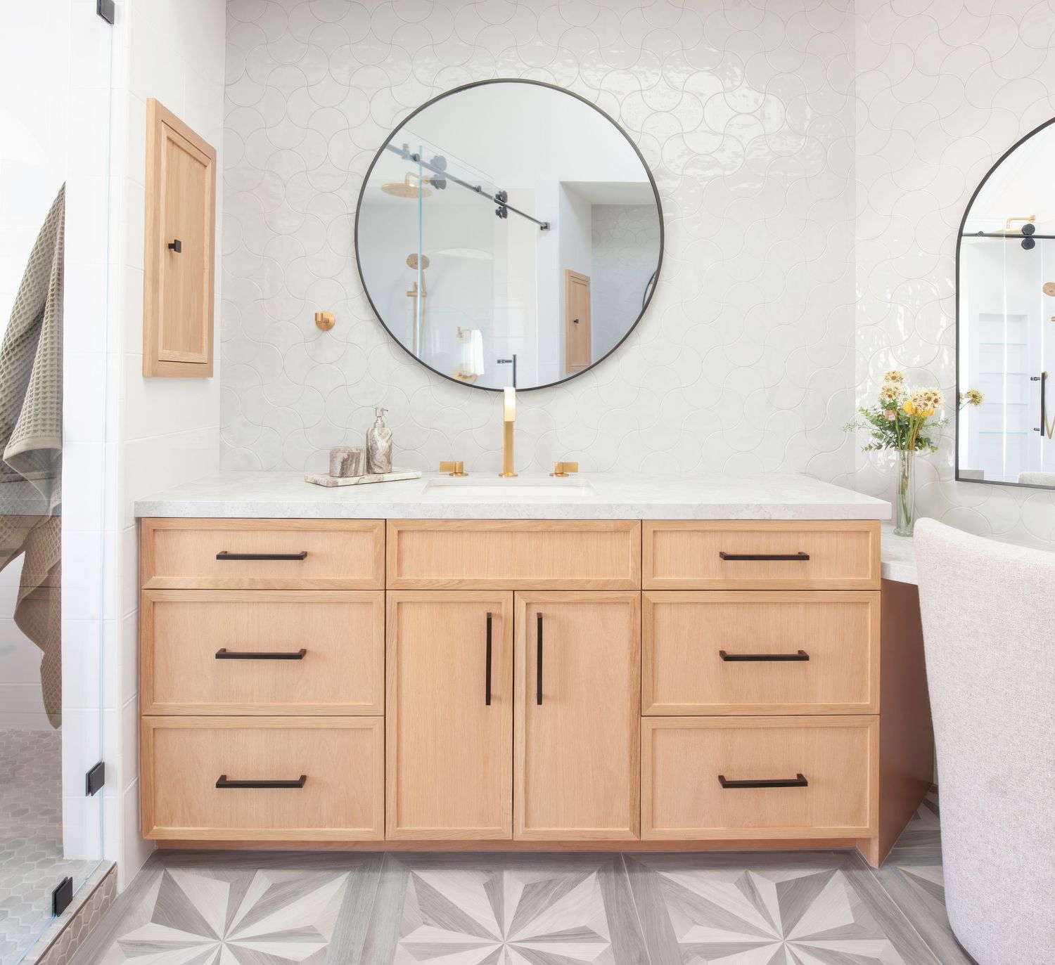 Interior photography of modern bathroom featuring round mirrors, wood vanity, and geometric floor tile pattern.