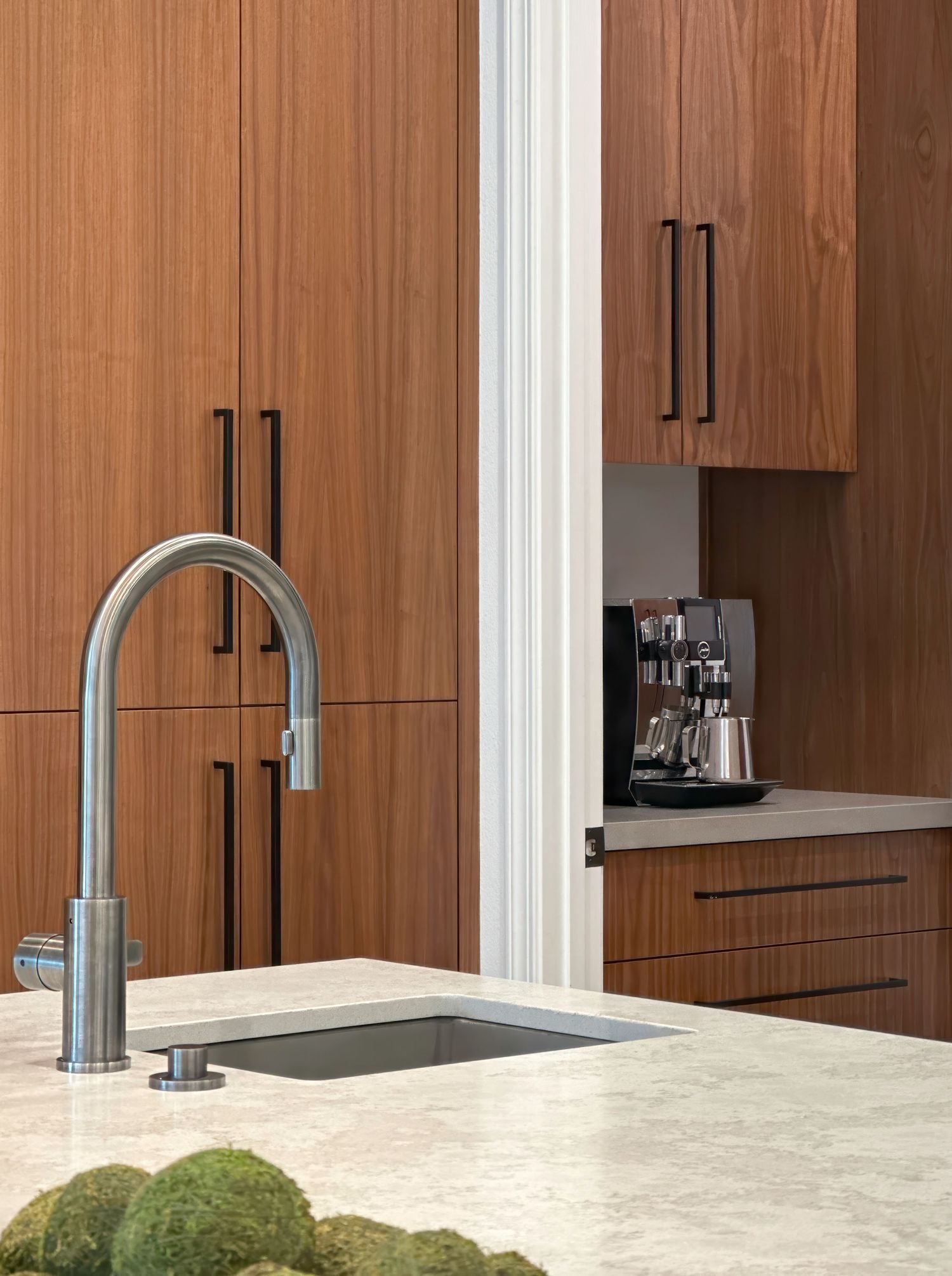 Close up photography of interior design kitchen vignette, showing wood cabinetry and white quartz countertop with modern faucet.