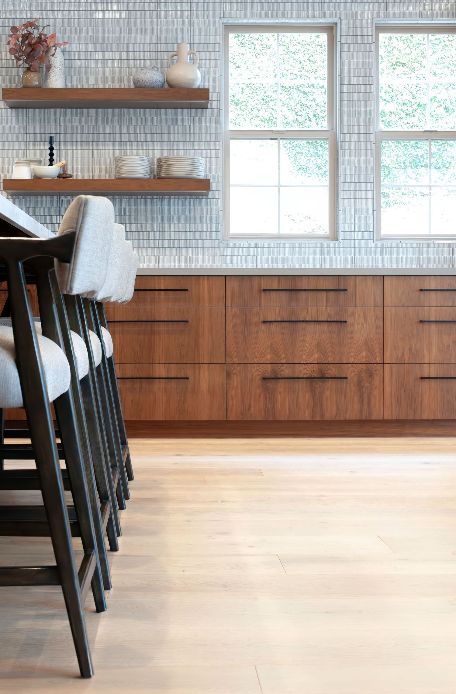 Modern kitchen with light wood flooring, custom wooden cabinets, and floating shelves against soft blue tile walls.