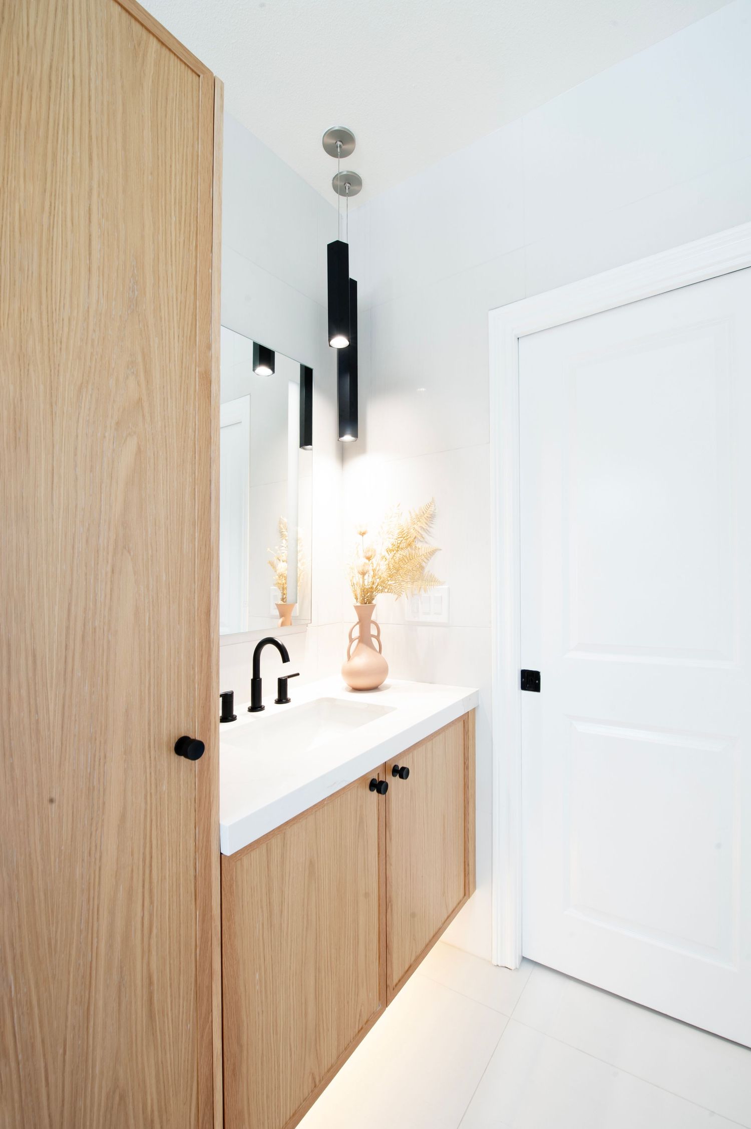 Sleek bathroom vanity with wooden cabinets, black pendant lights, and dried floral arrangement.