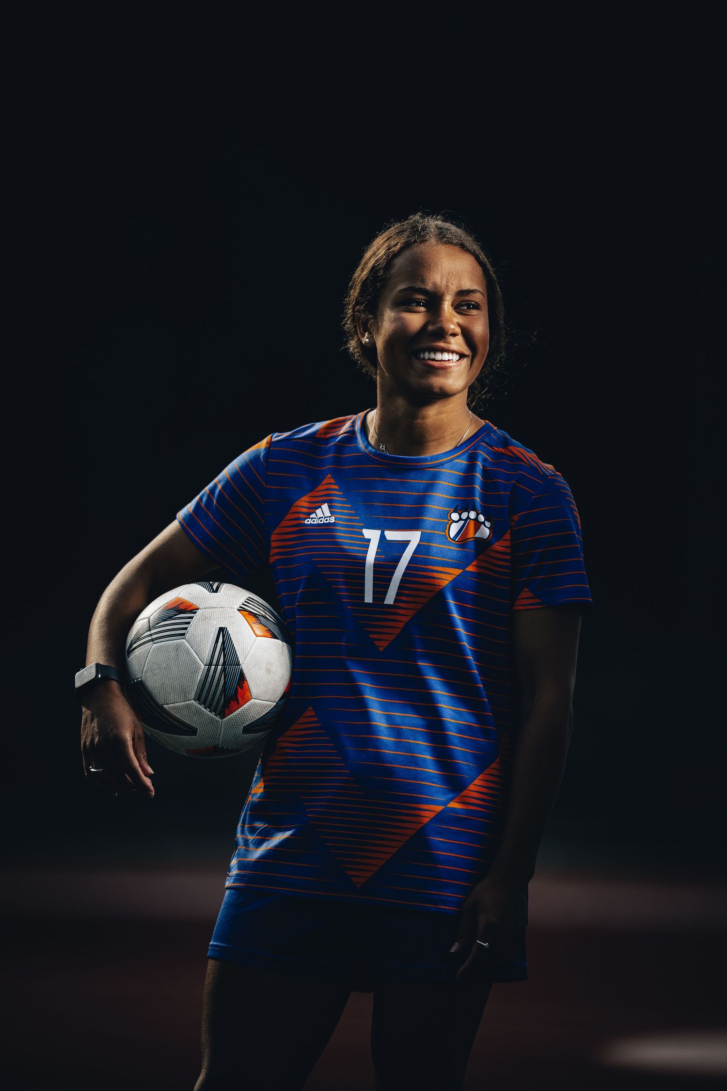 Soccer player in blue striped jersey poses with official match ball.