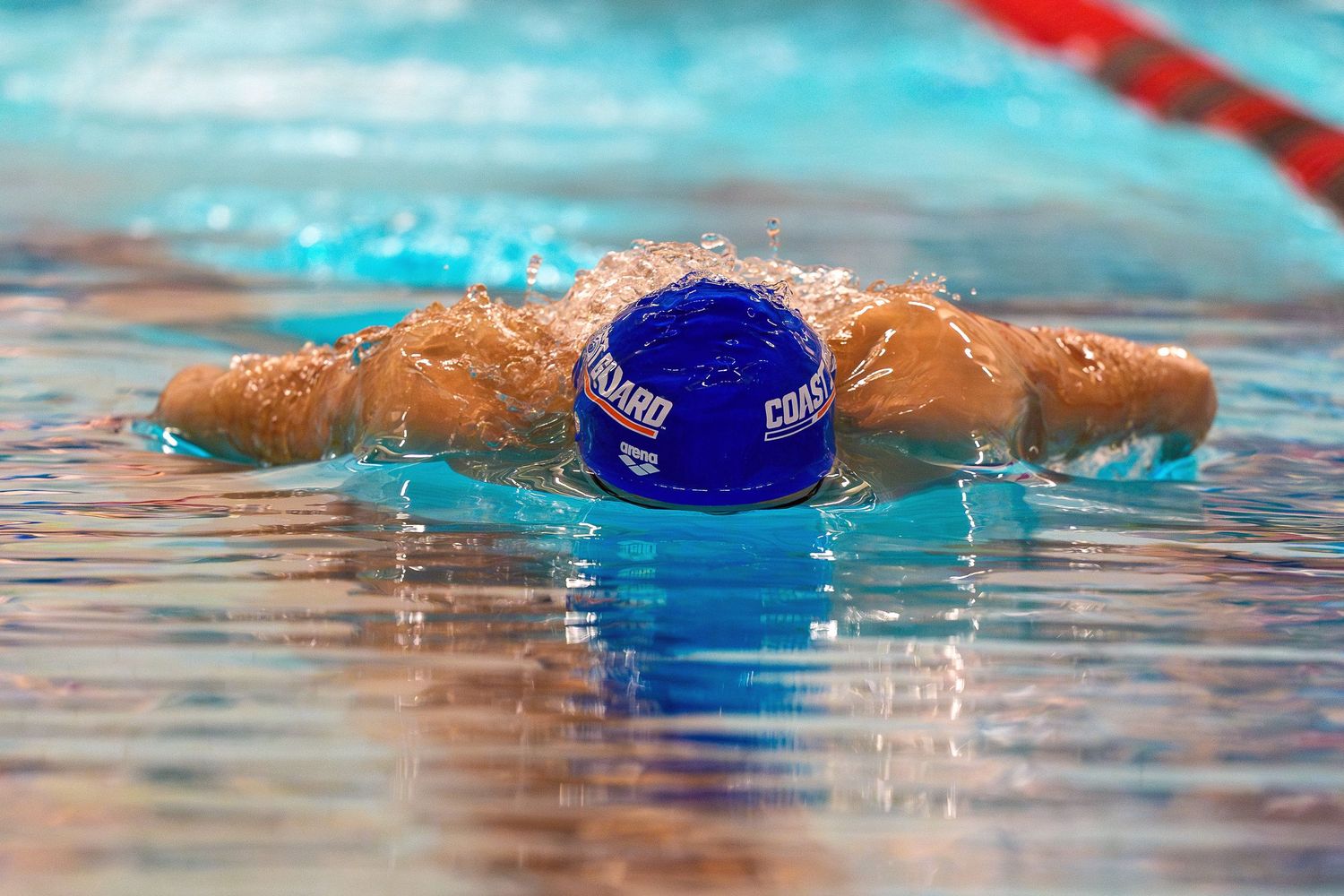 A swimmer wearing a blue cap performs the butterfly stroke during a competitive race in a pool.