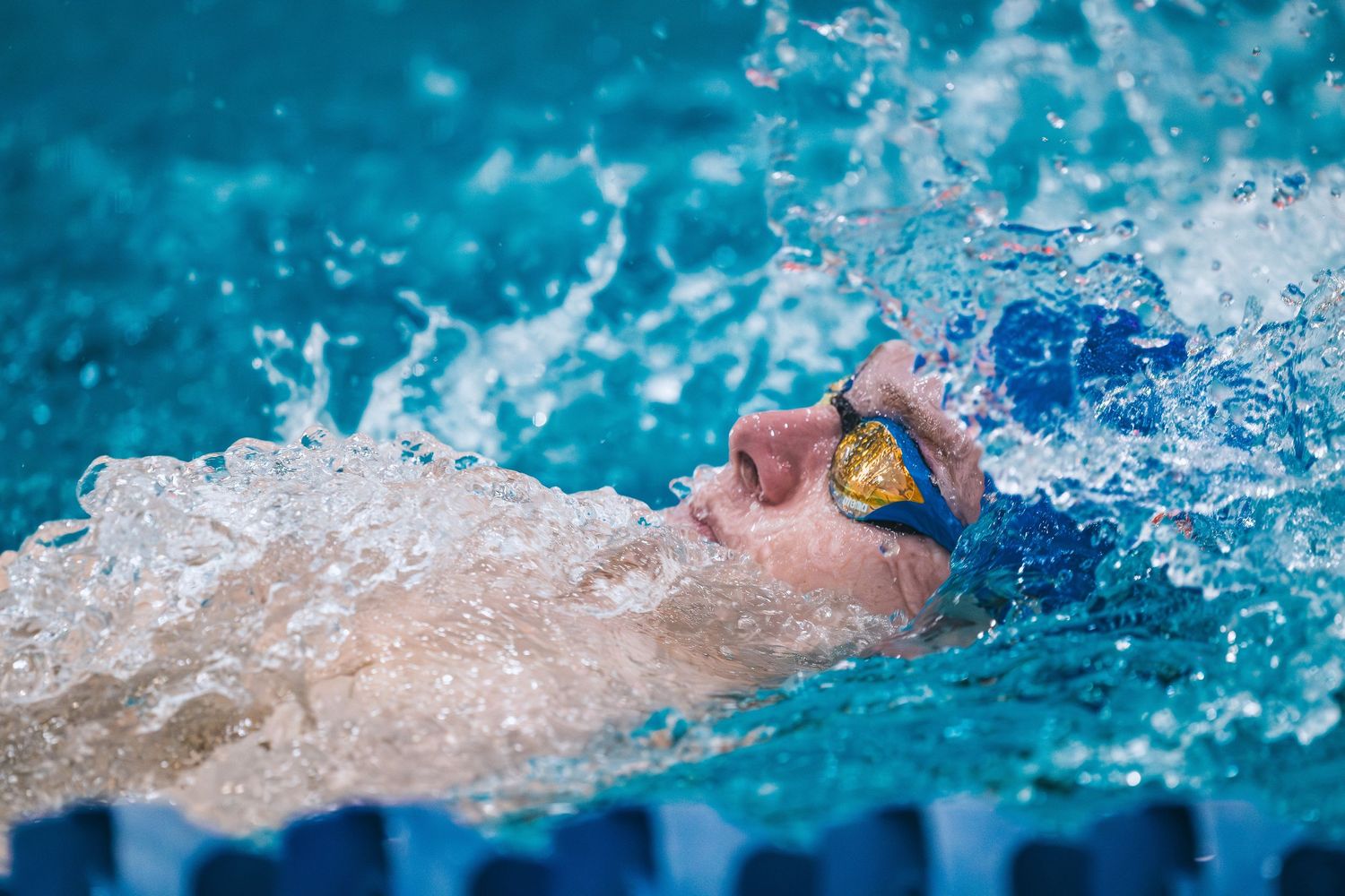 Close-up of swimmer doing backstroke with water splashing around goggles.