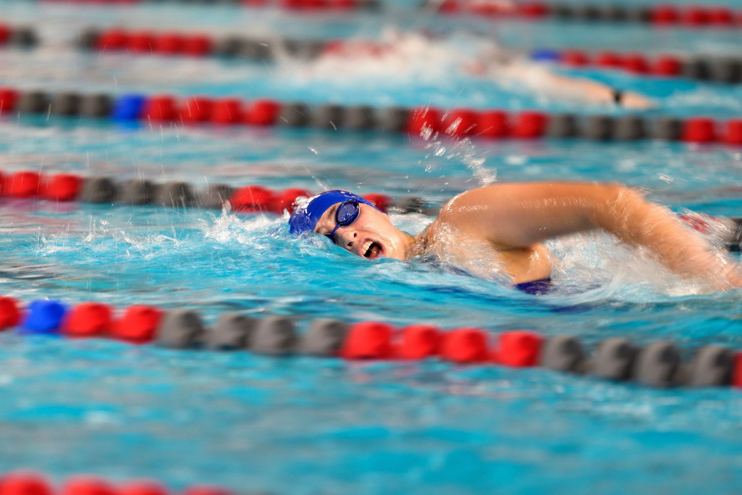 Swimmer performs freestyle stroke in a competition pool with red and blue lane dividers.