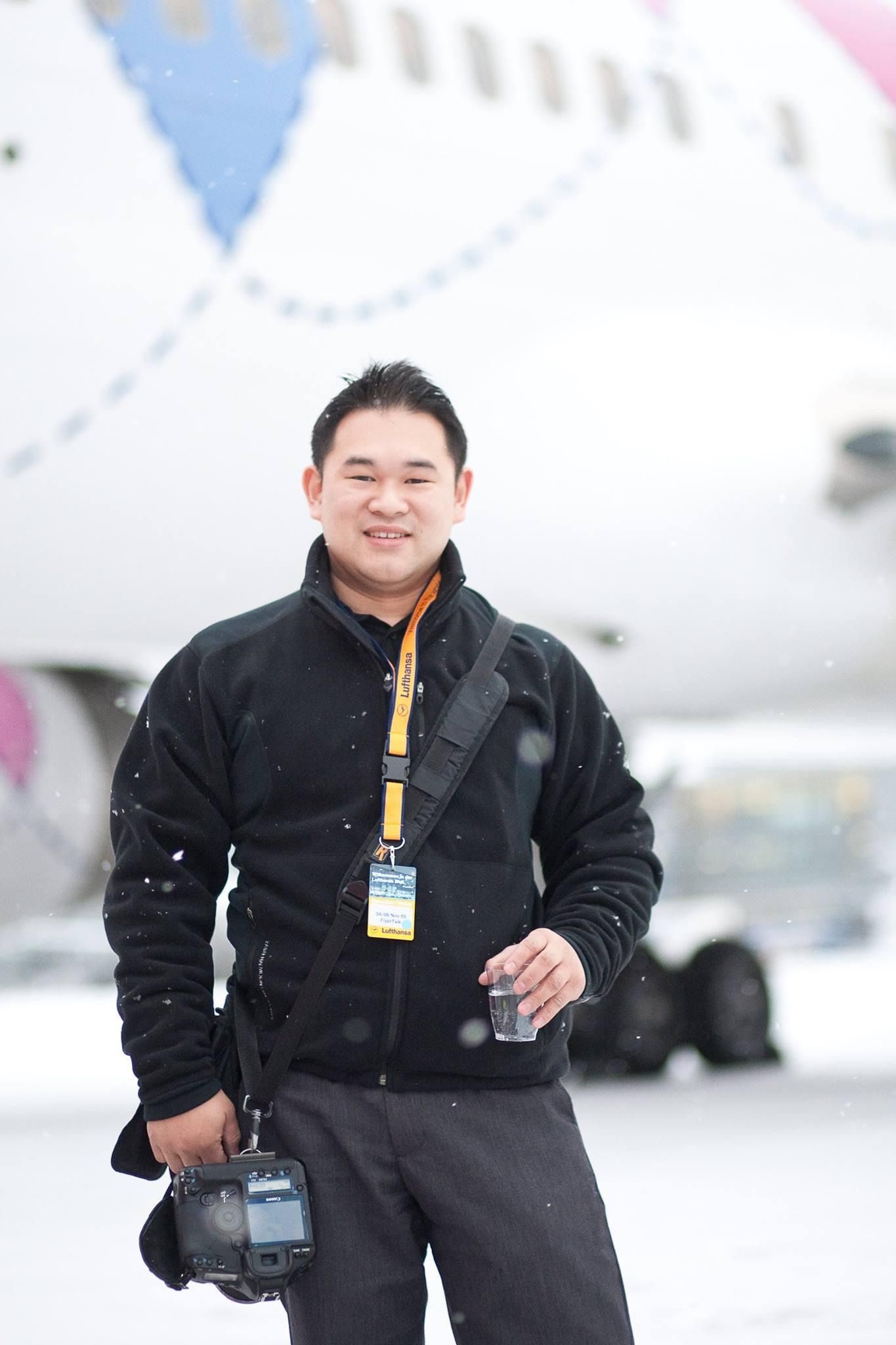 Person in black jacket holding camera equipment in snowy conditions near an aircraft.