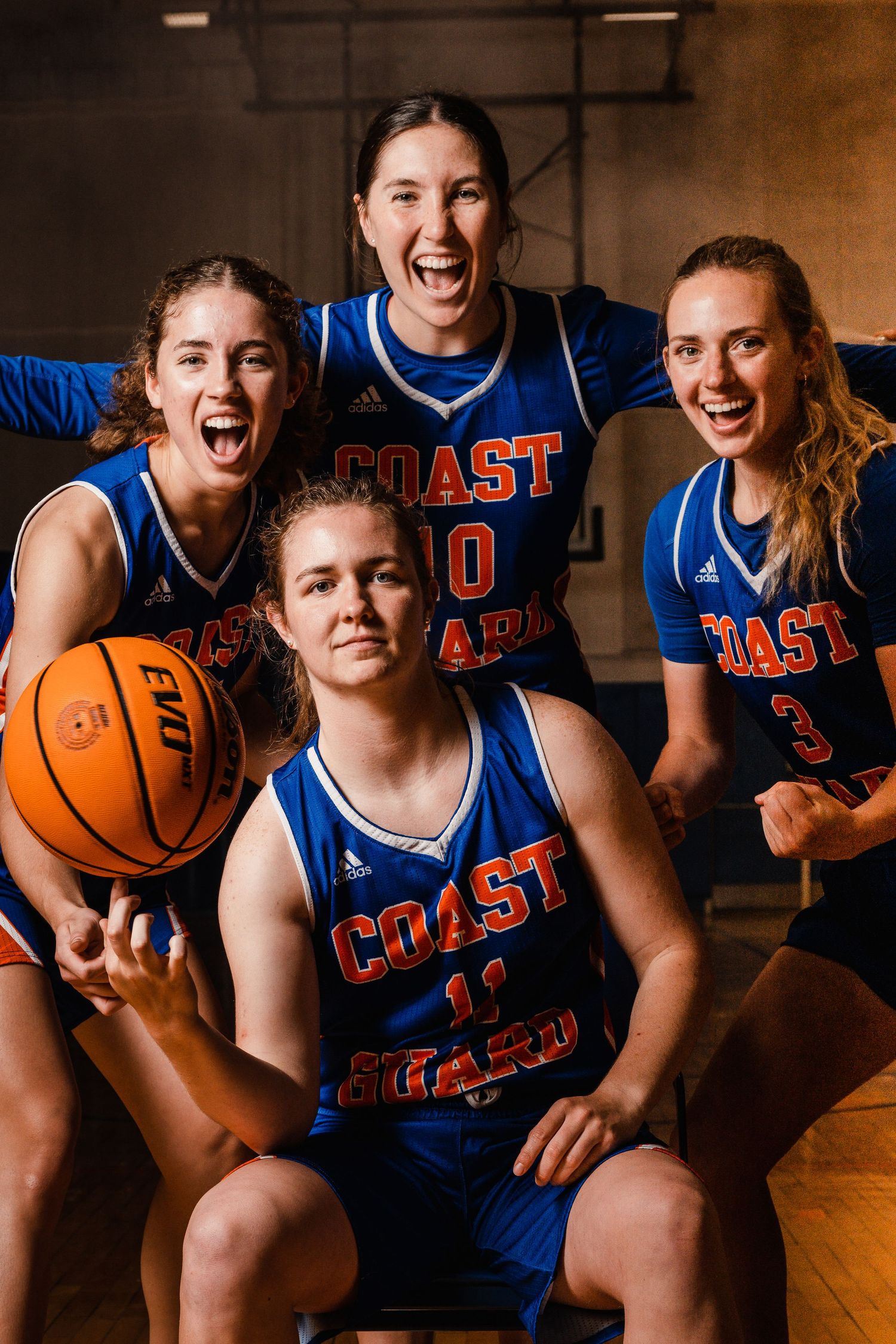 College basketball team members in Coast Guard uniforms pose together with basketballs.