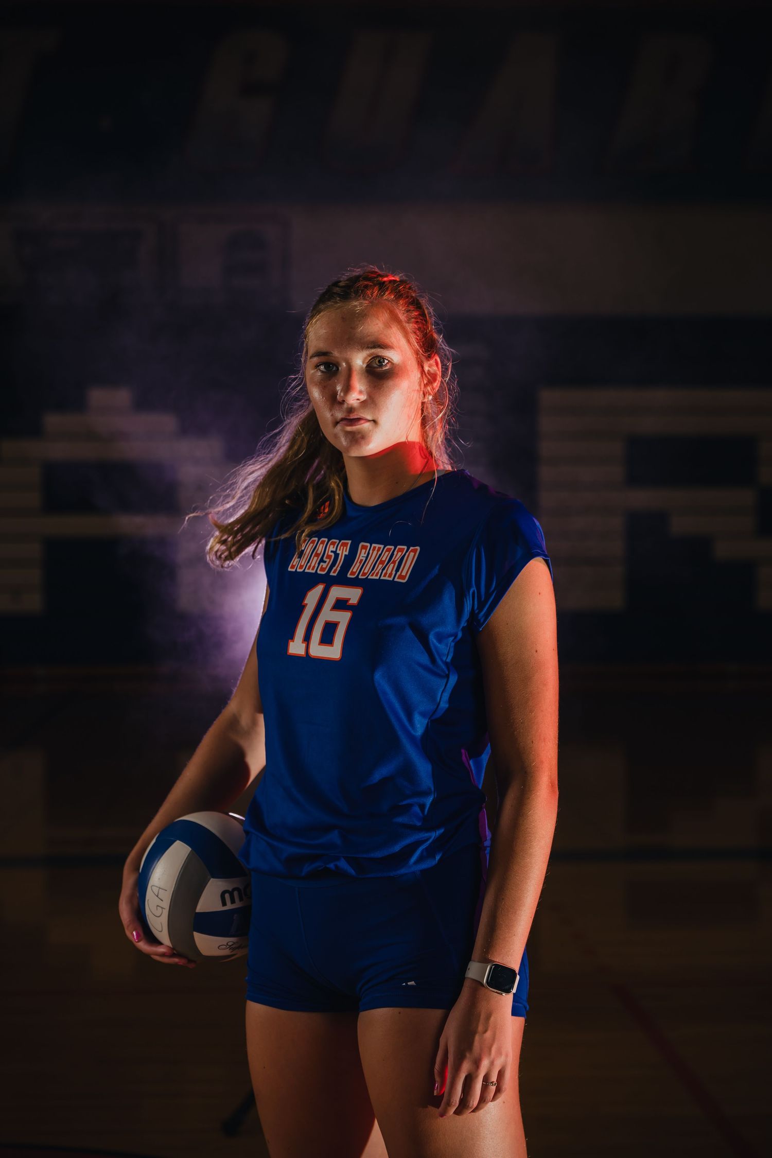 Athlete in blue jersey holds volleyball in dramatic indoor sports portrait with moody lighting.