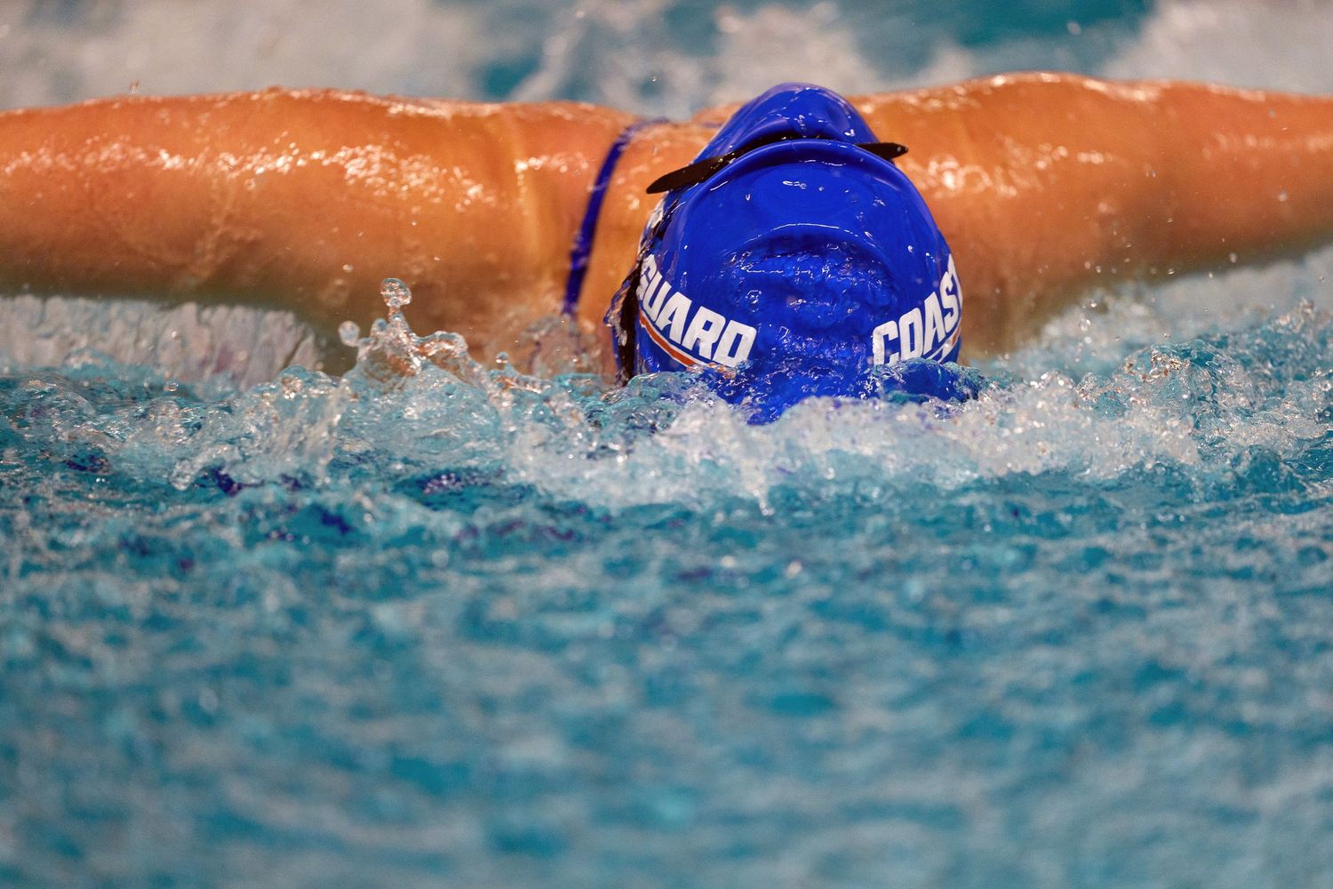 Close-up of swimmer in blue cap performing butterfly stroke in pool.