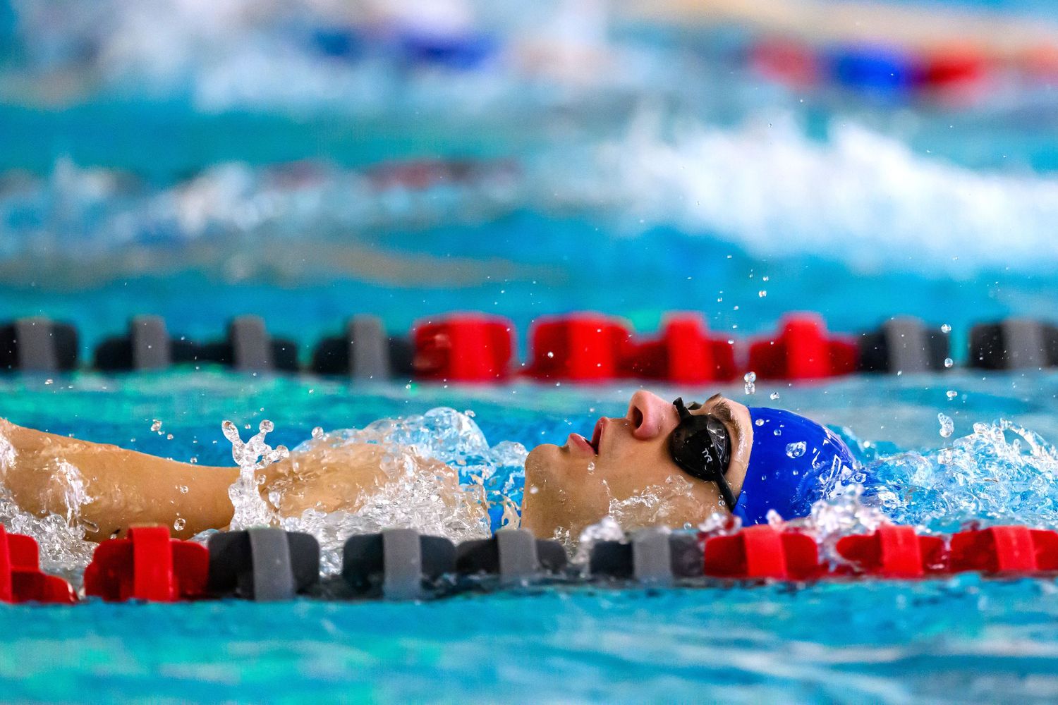Swimmer in blue racing suit performs backstroke in a competitive pool.
