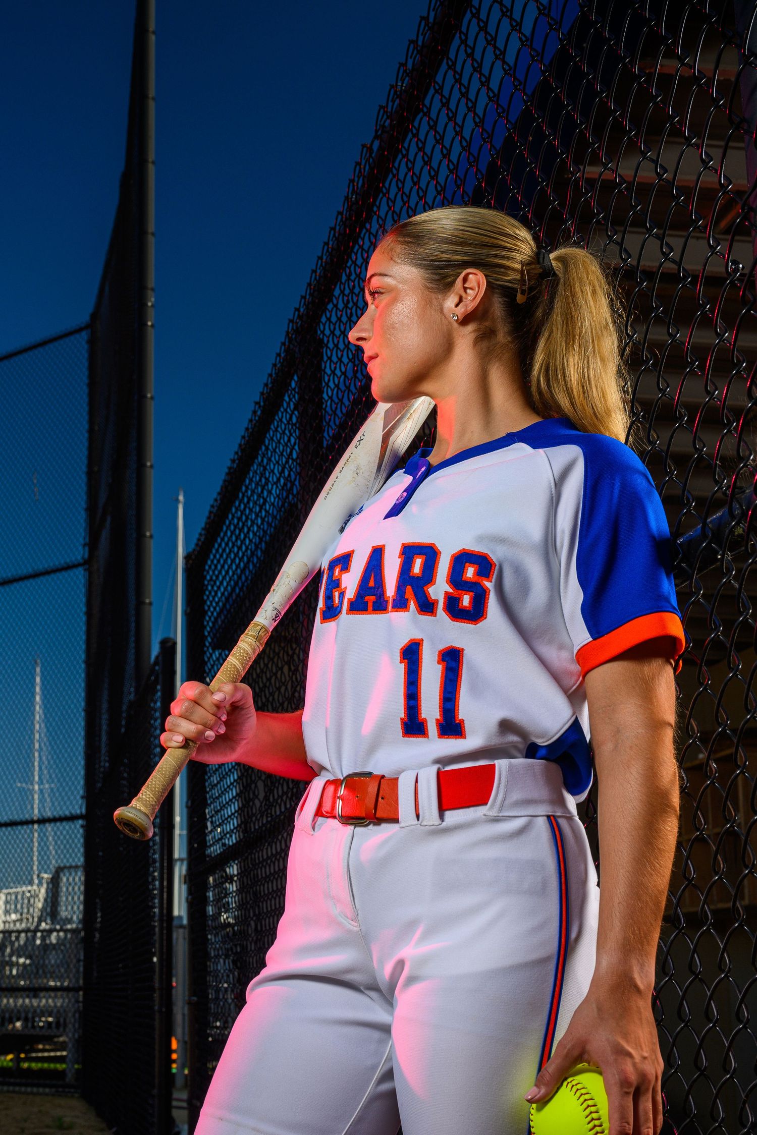 A baseball player in Bears uniform stands against fence holding bat in athletic stance.