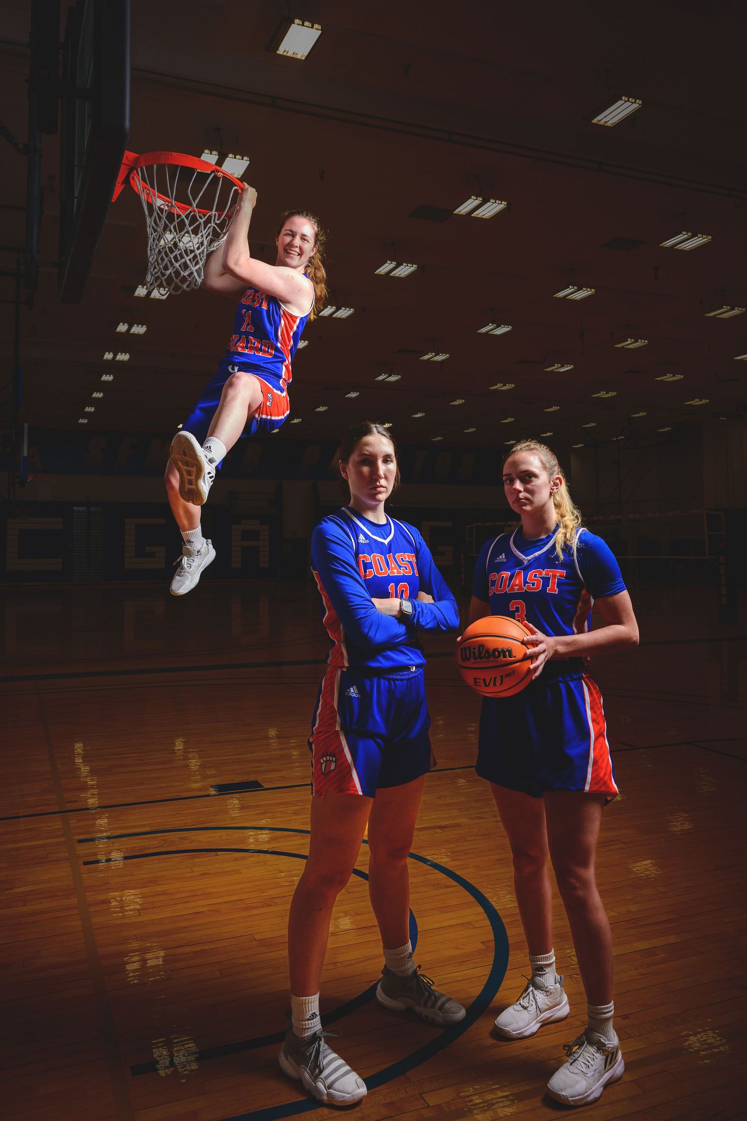 Basketball players in blue uniforms pose for dynamic team photo with one player dunking.