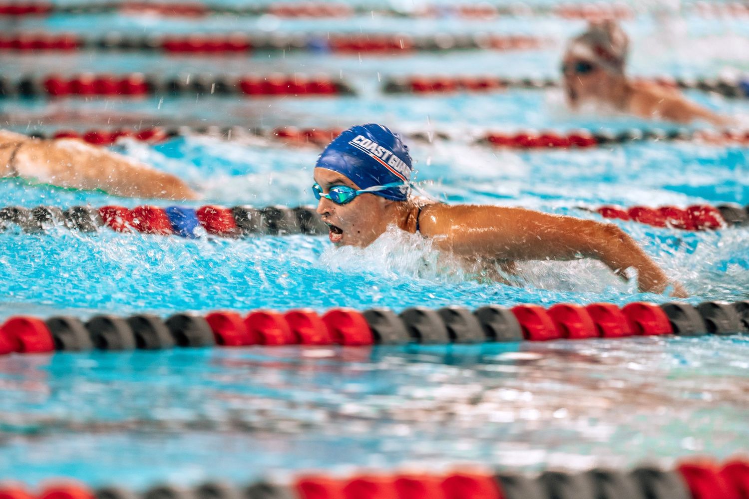 Competitive swimmer performs butterfly stroke in a lap pool with red and white lane dividers.