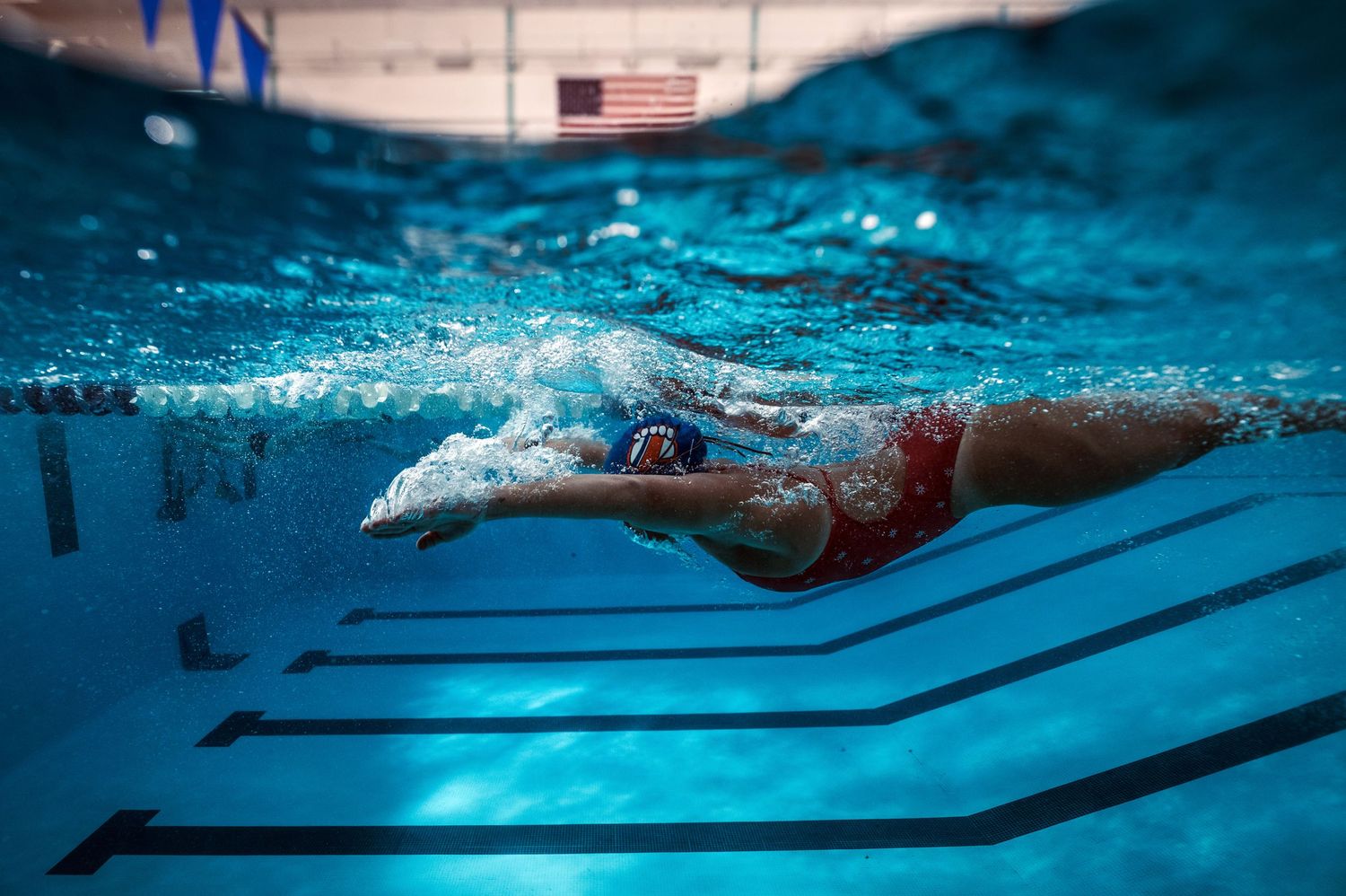 Underwater view of swimmer performing freestyle stroke in crystal clear pool water.