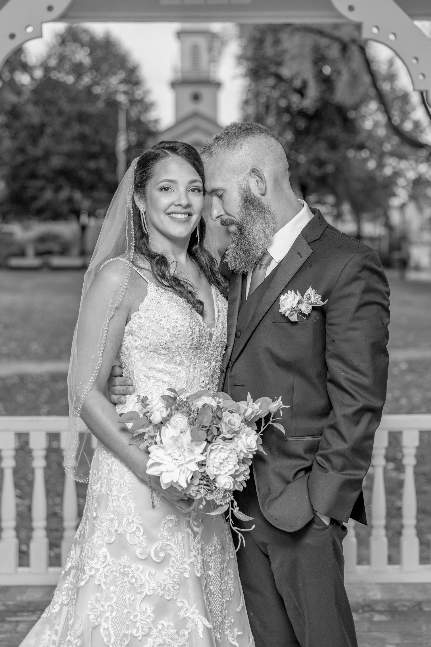 Romantic black and white portrait of a couple in wedding attire on a gazebo.