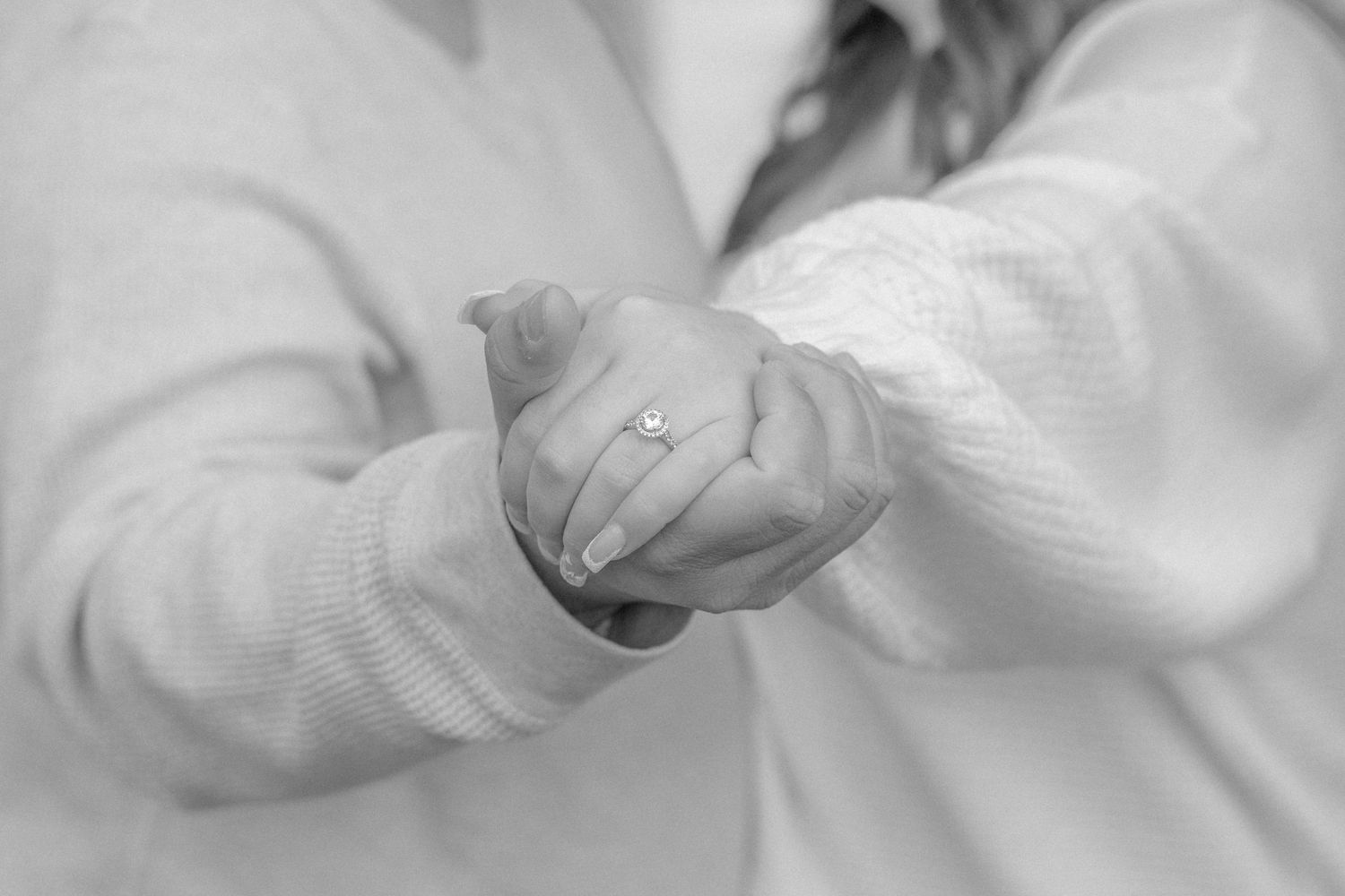 A close-up black and white photo of hands with an engagement ring.