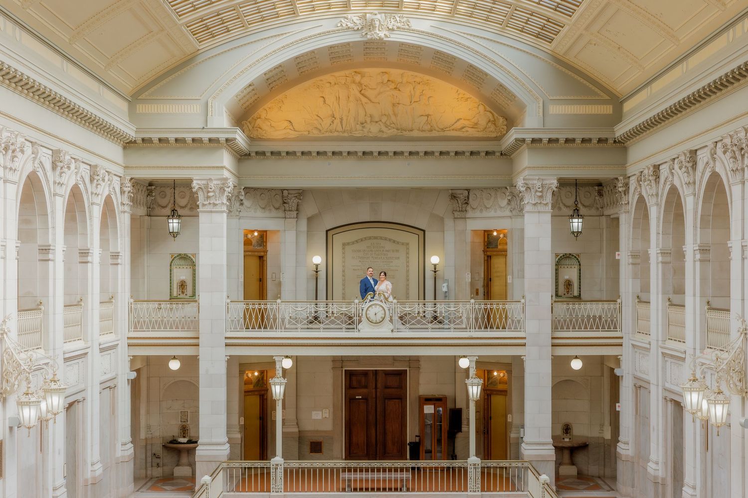 A grand marble hall with ornate architecture and balconies captures an intimate wedding moment.