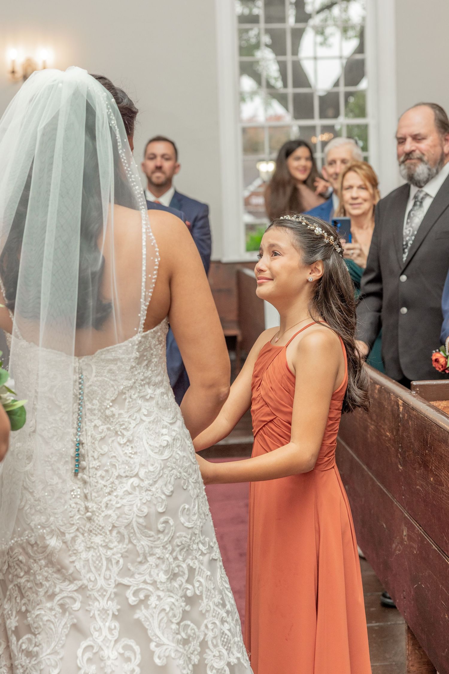 Young attendant in coral dress watches ceremony from church pew.