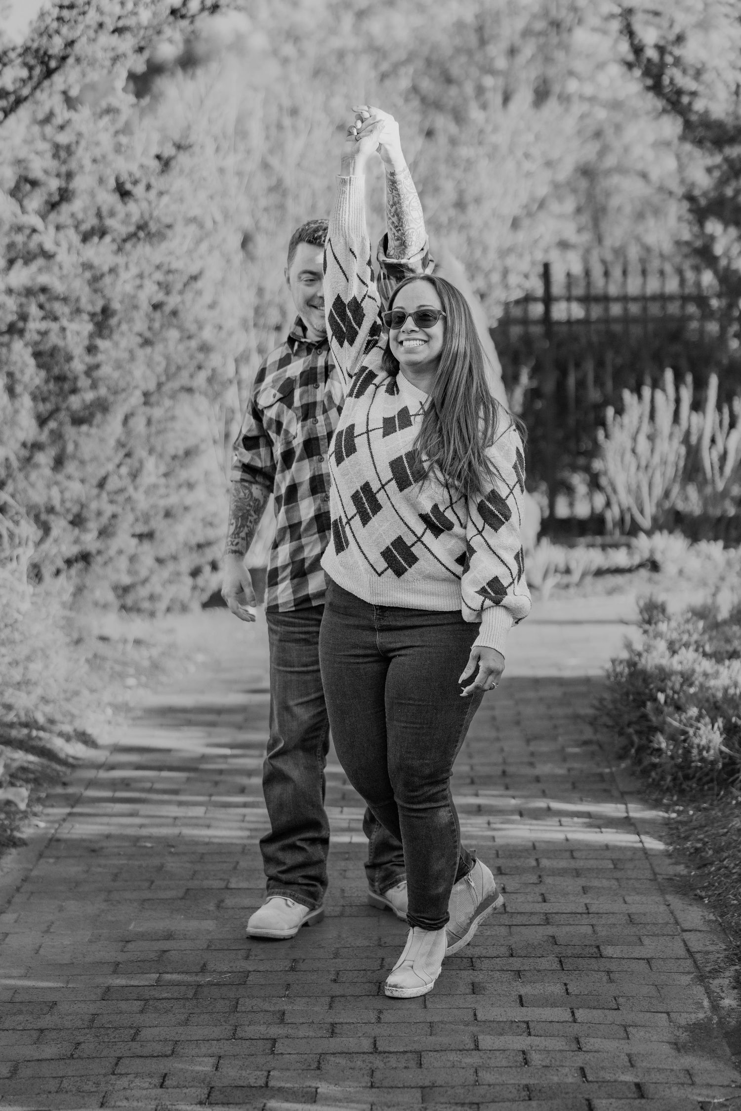 Couple in matching plaid shirts posing on brick path while holding hands in black and white photo.