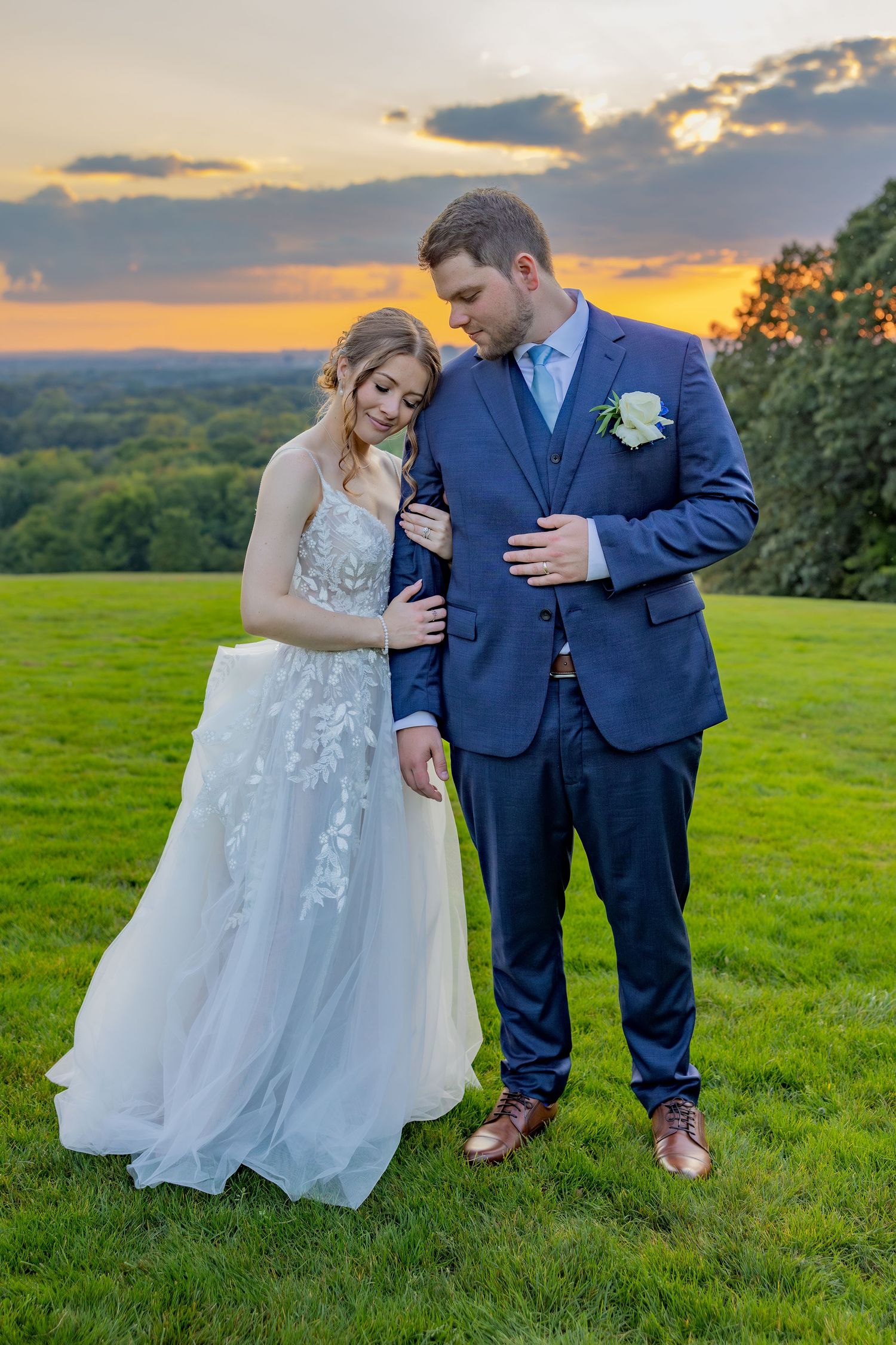 Sunset wedding portrait on a hilltop with dramatic sky and rolling landscape in background.