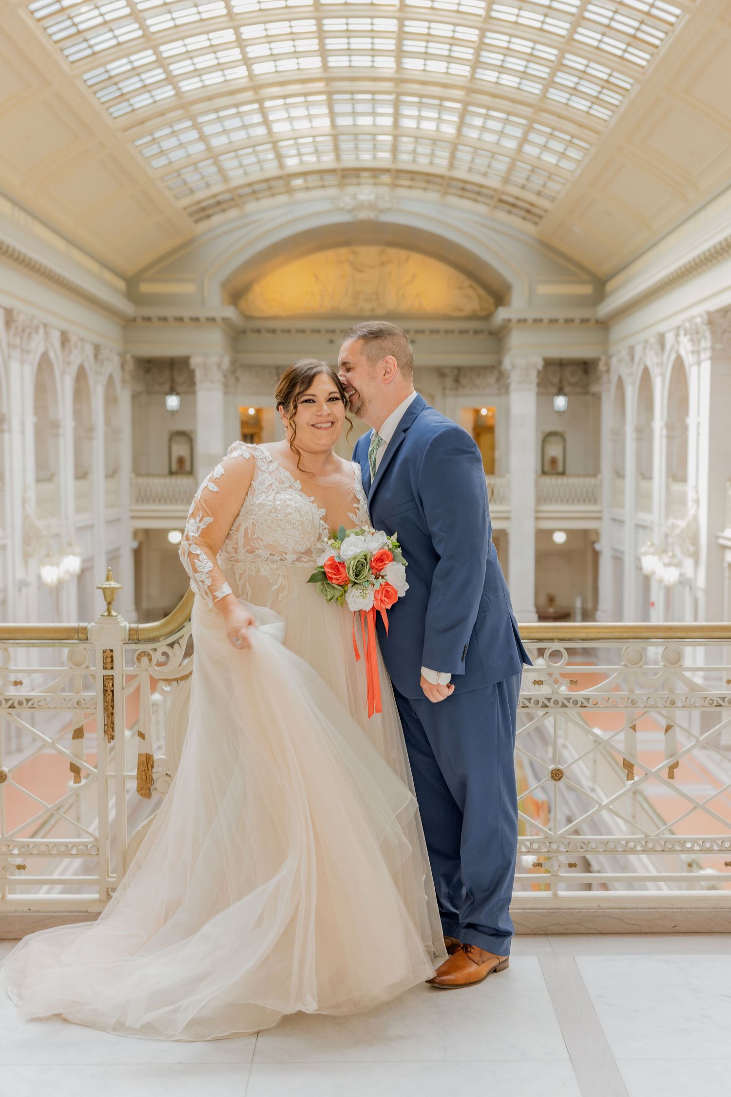 Couple shares intimate moment in grand marble hall with skylight ceiling during wedding photoshoot.