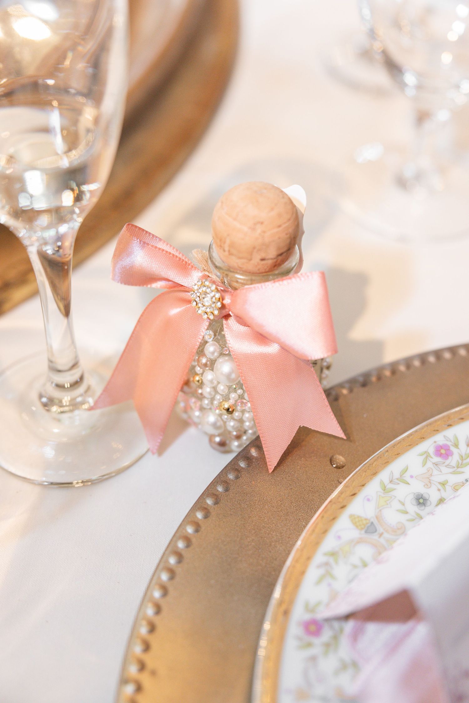 Wedding table detail with pink bow and pearl accents on gold-rimmed place setting.