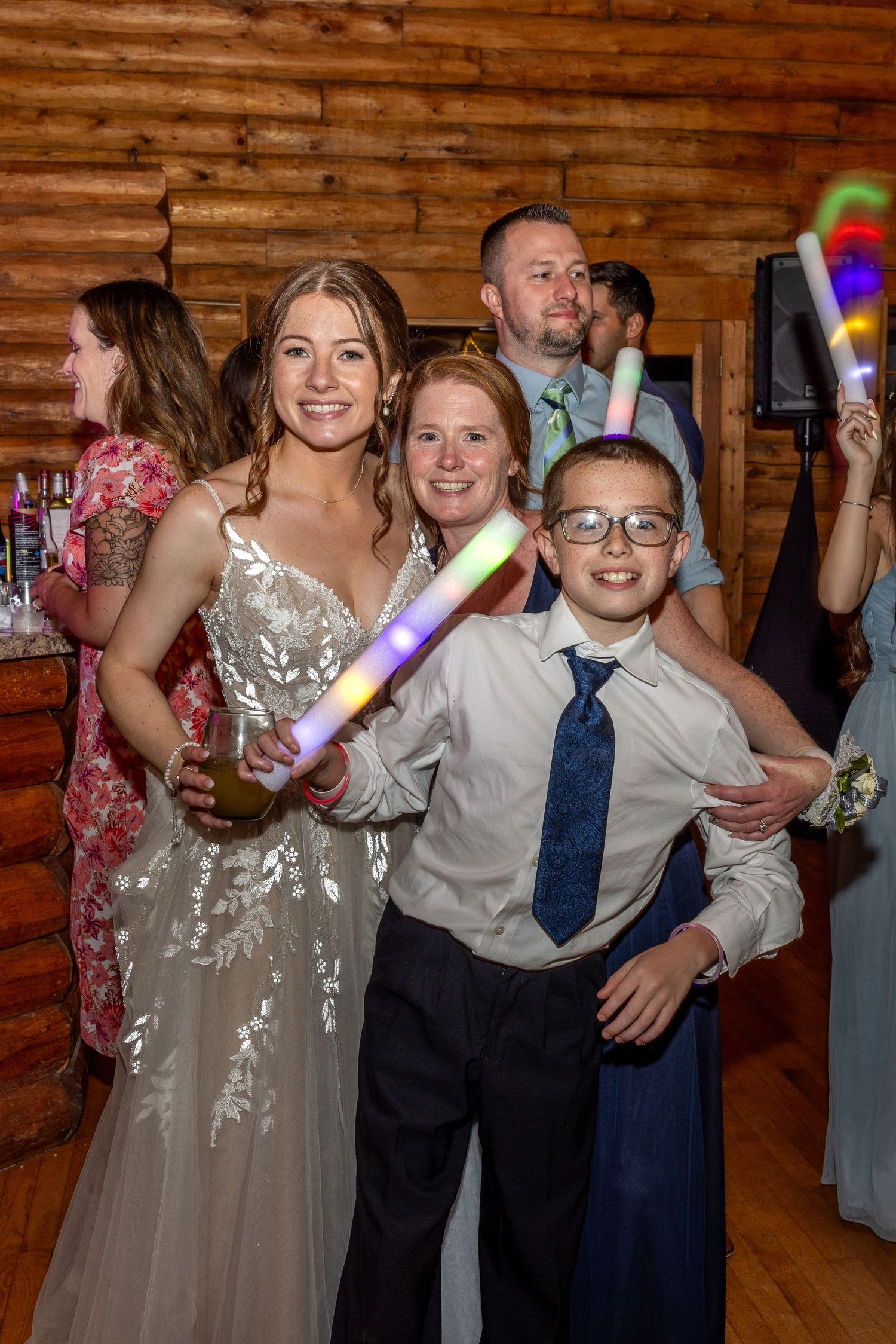 Reception celebration in a rustic wooden venue with light-up party favors and joyful dancing.