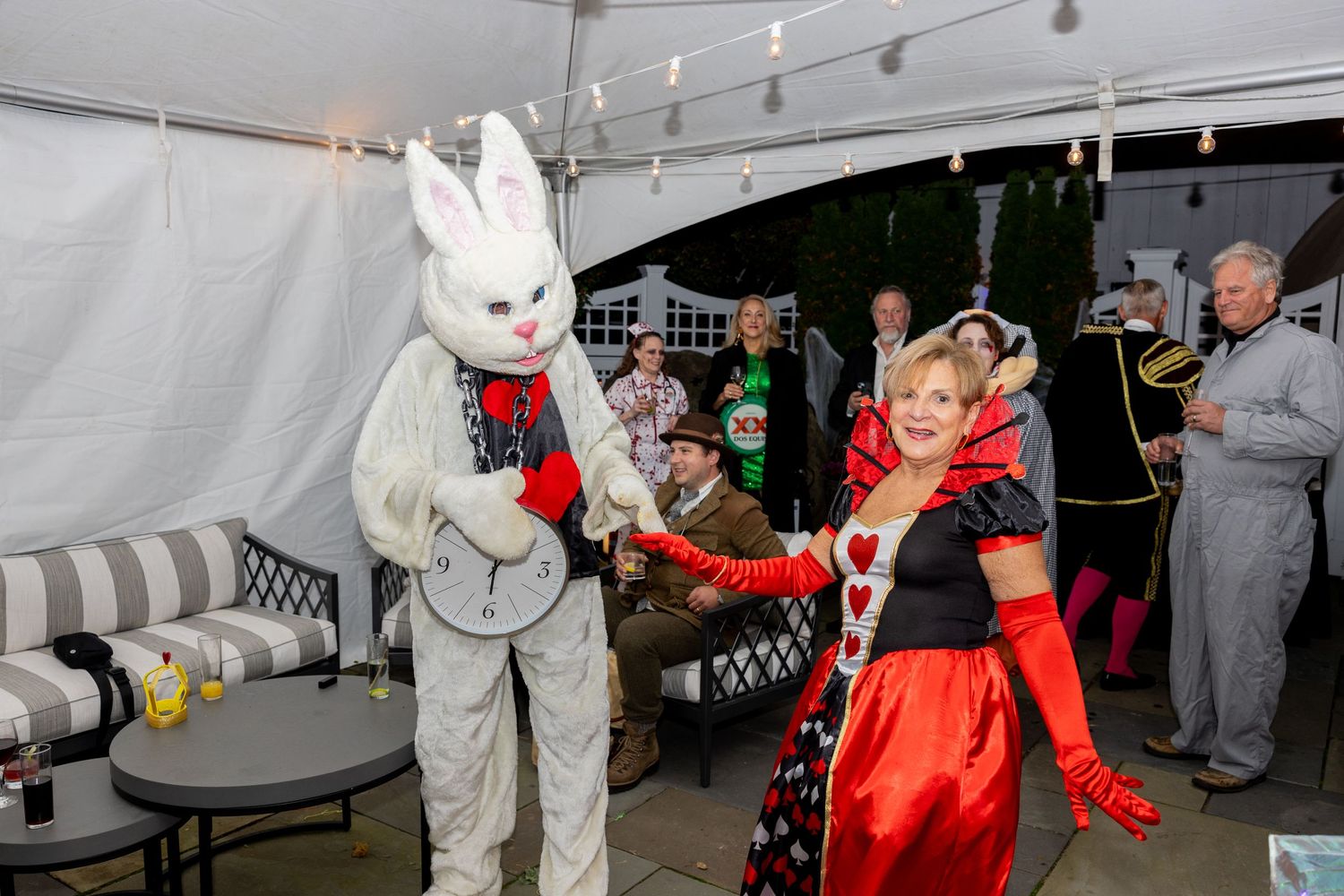 A costumed bunny character dances with someone in a red outfit under a party tent with string lights.