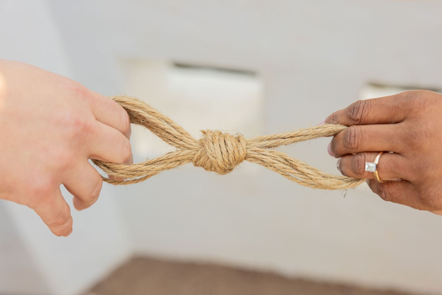 Two hands pulling opposite ends of a tied rope knot against a white background.