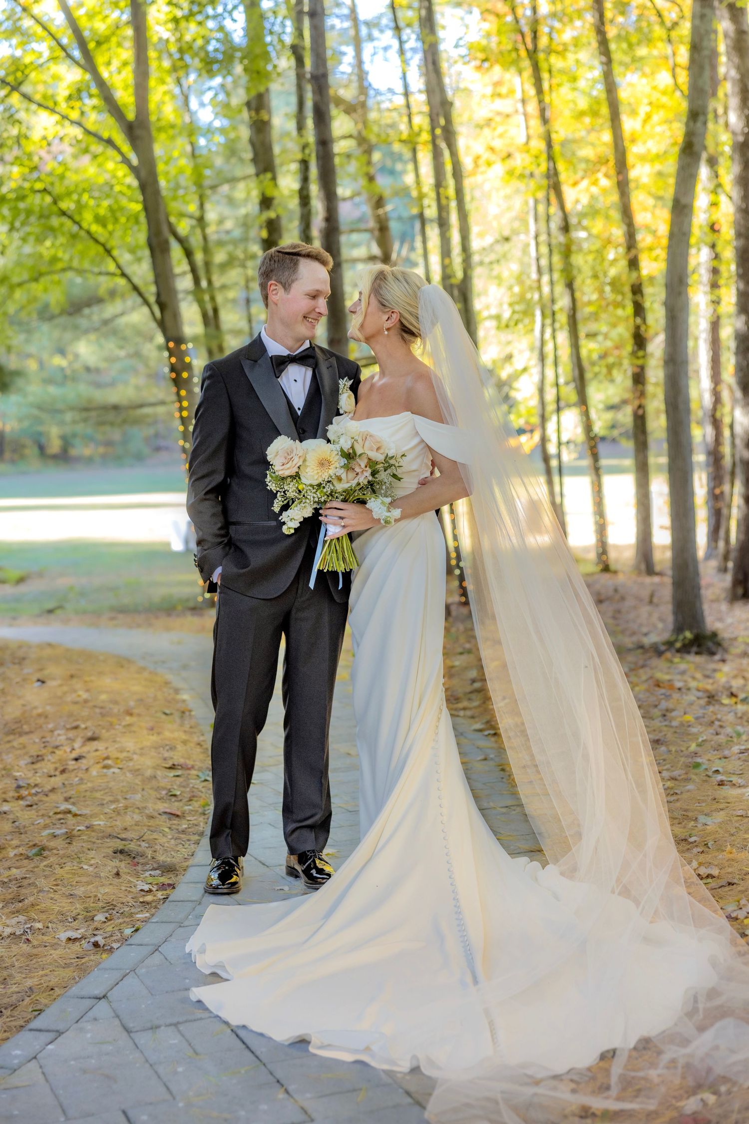 Elegant couple poses in autumn forest with bride holding white bouquet.