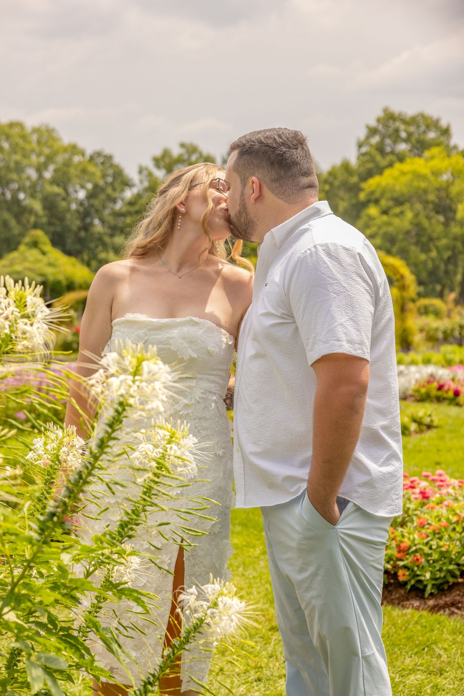A romantic moment shared between a couple in a vibrant flower garden with white and pink blooms.