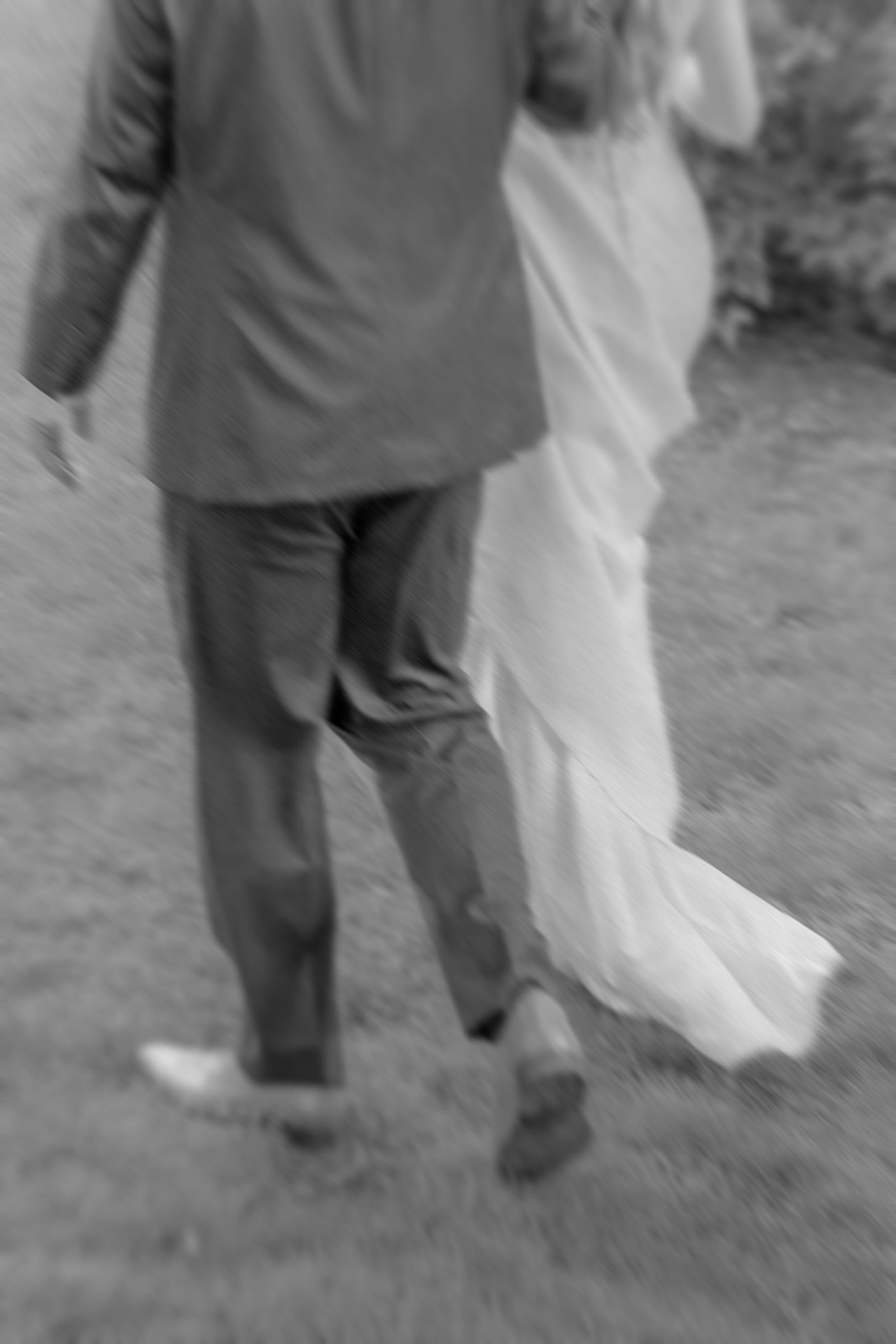 A blurred black and white photograph shows the lower half of a couple at a wedding, with flowing dress and suit pants.