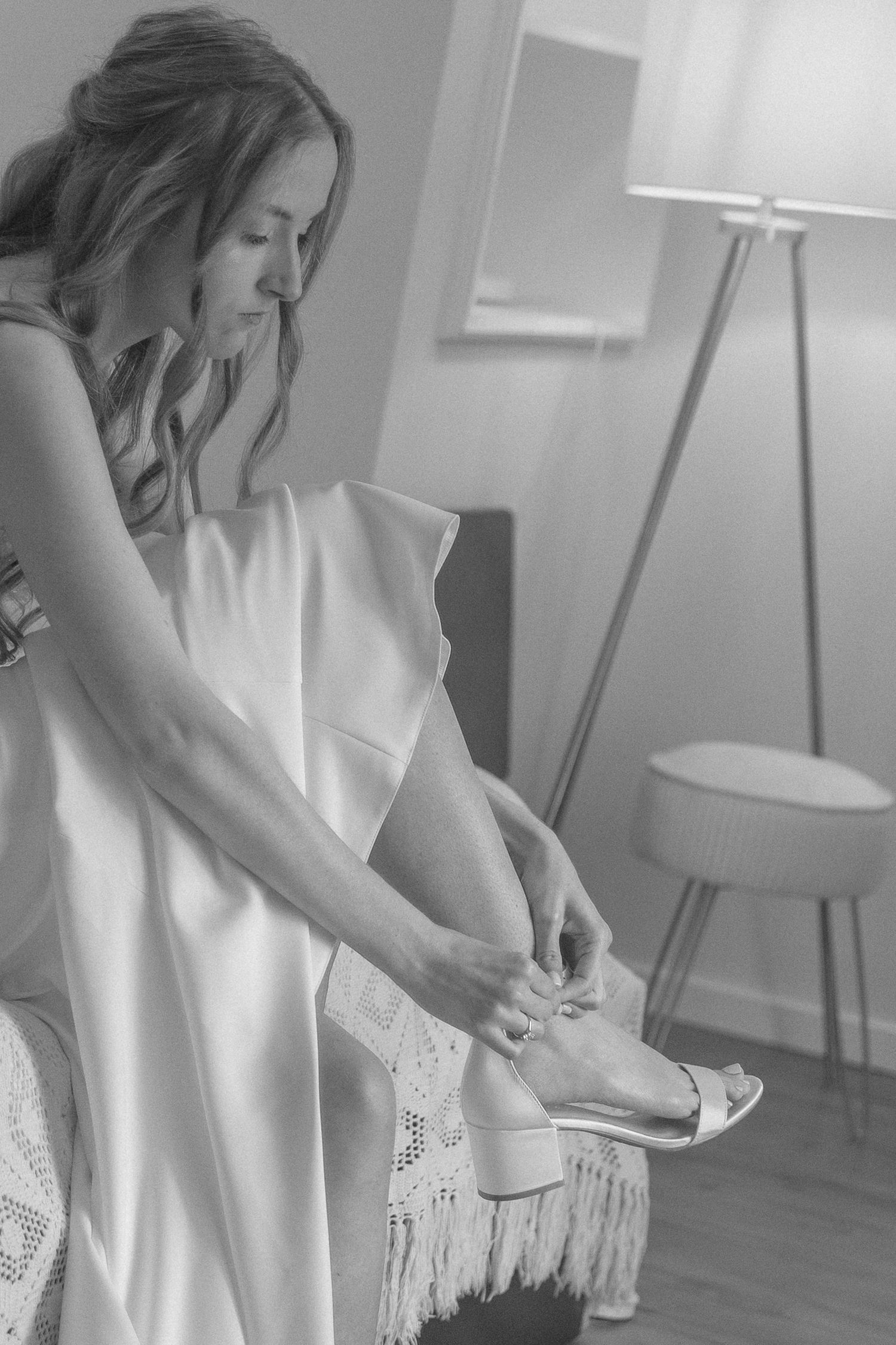 A woman in a white dress adjusts her ballet slipper in a black and white photo.