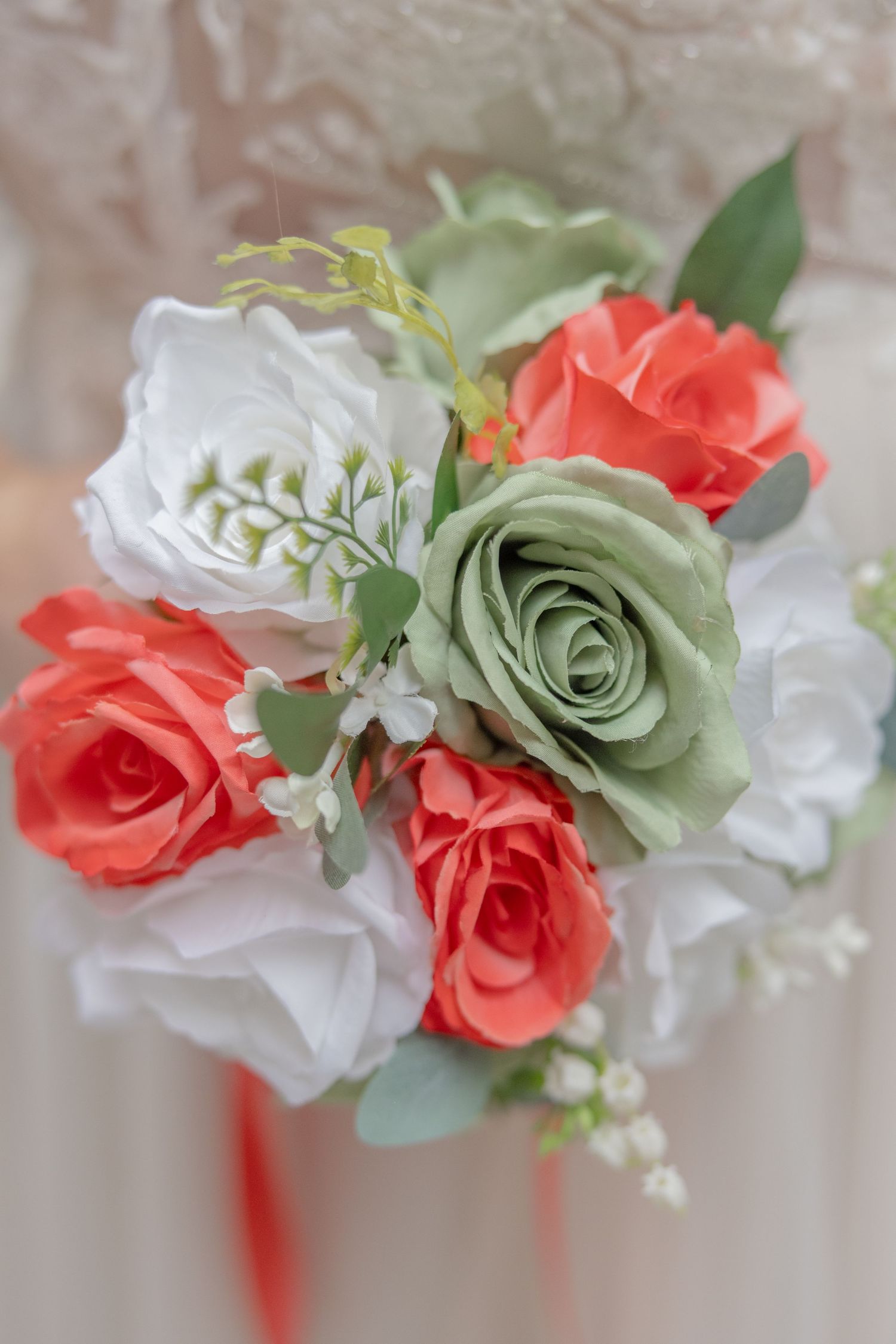 Wedding bouquet with coral, white and sage green roses against soft background.