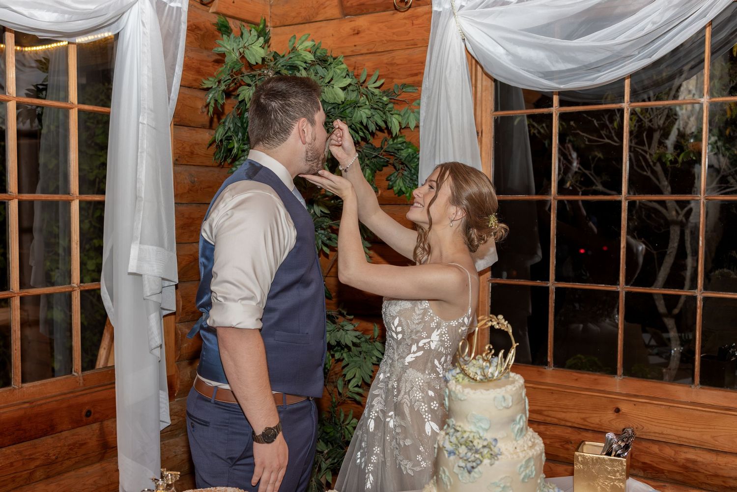 Couple shares playful moment while cutting their wedding cake in rustic wooden venue.