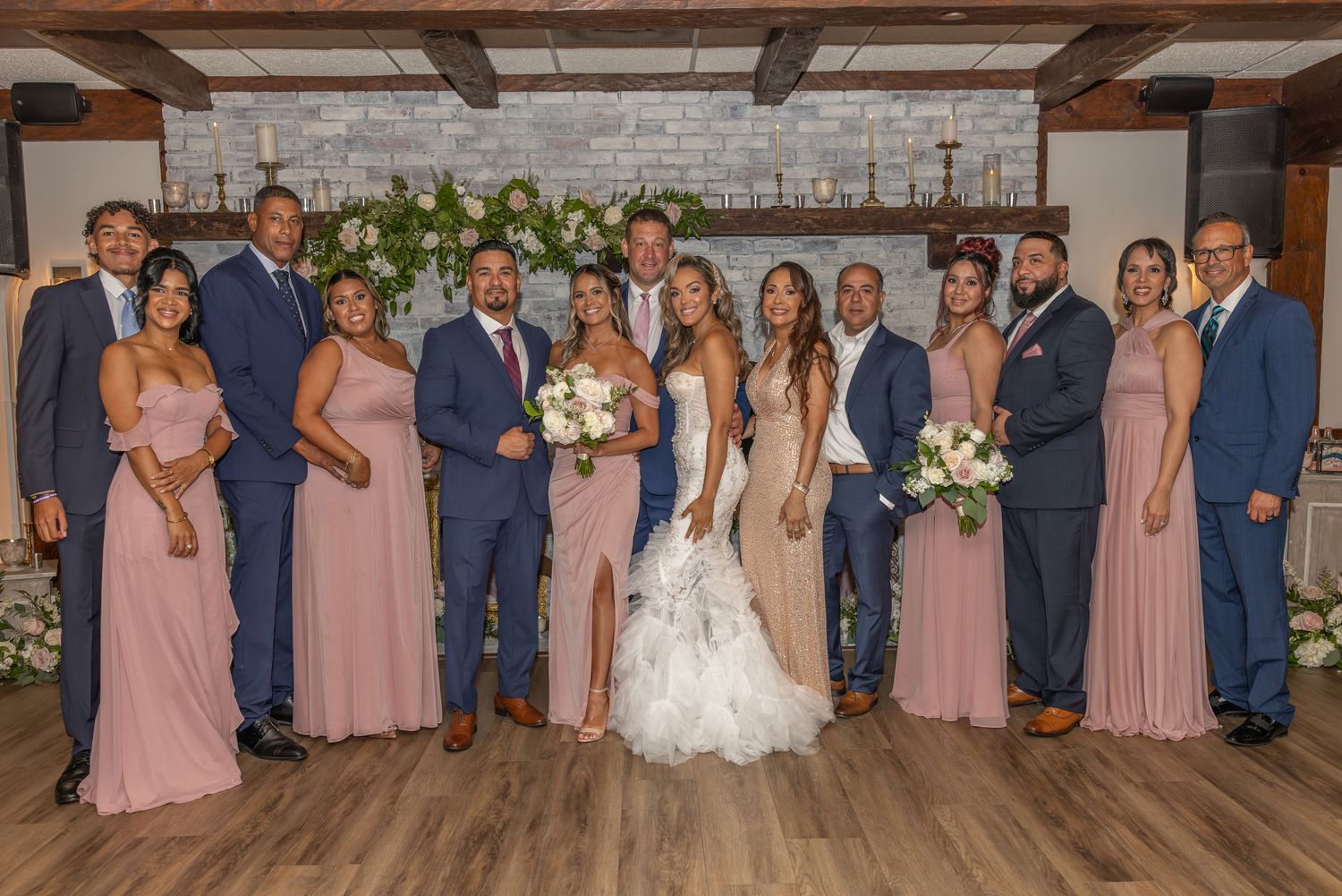 Full wedding party in navy suits and dusty rose dresses poses in rustic venue.