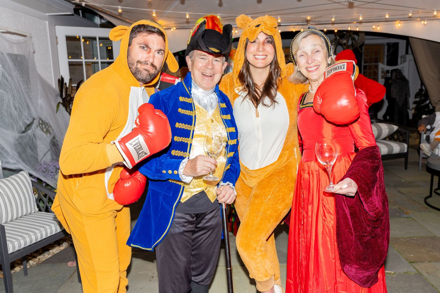 Group wearing colorful animal and character costumes pose with boxing gloves at party.