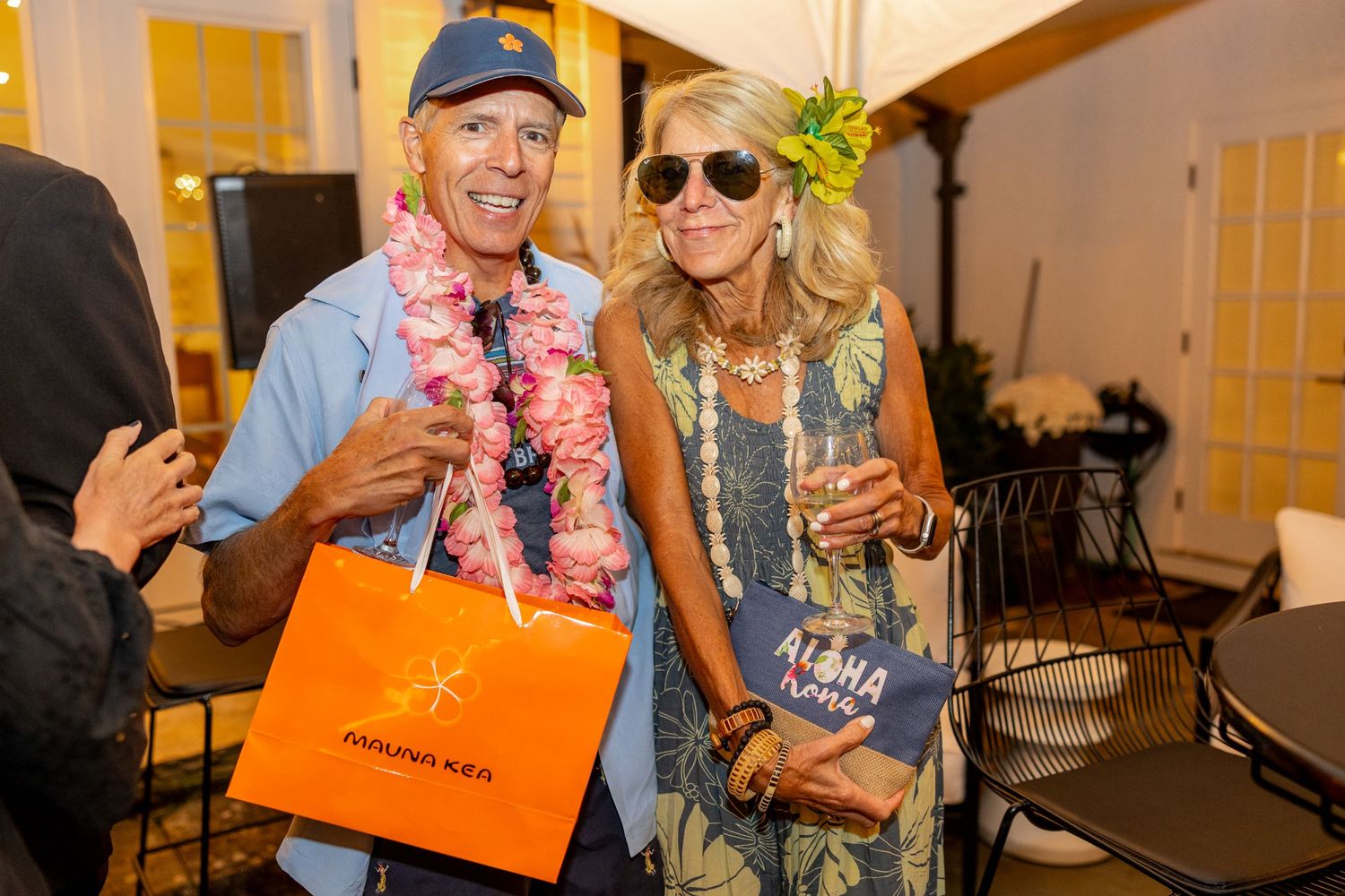 Party guests in tropical attire and leis pose with gift bags at indoor event.