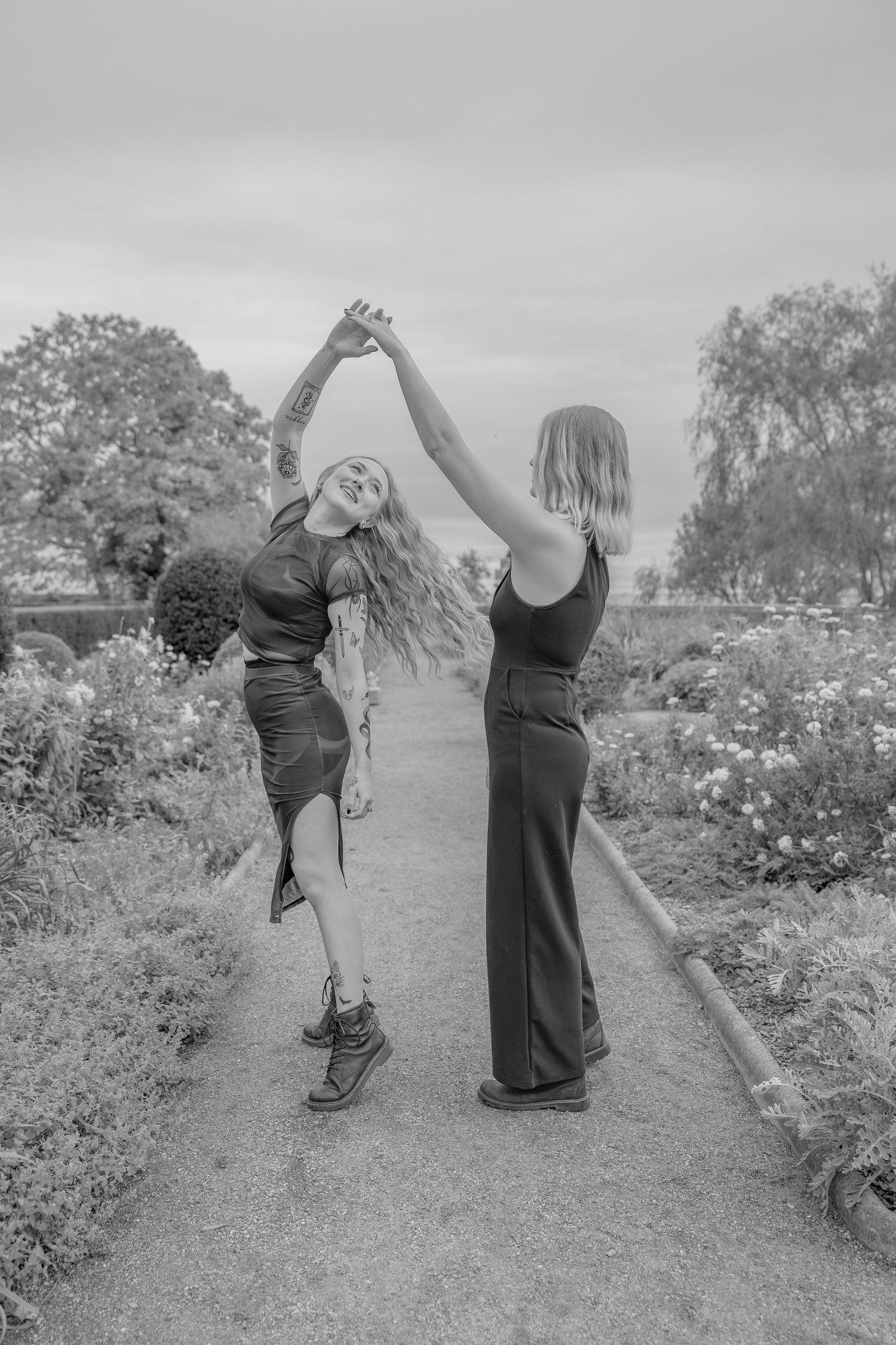 Two people dancing joyfully on a garden path in black and white photography.