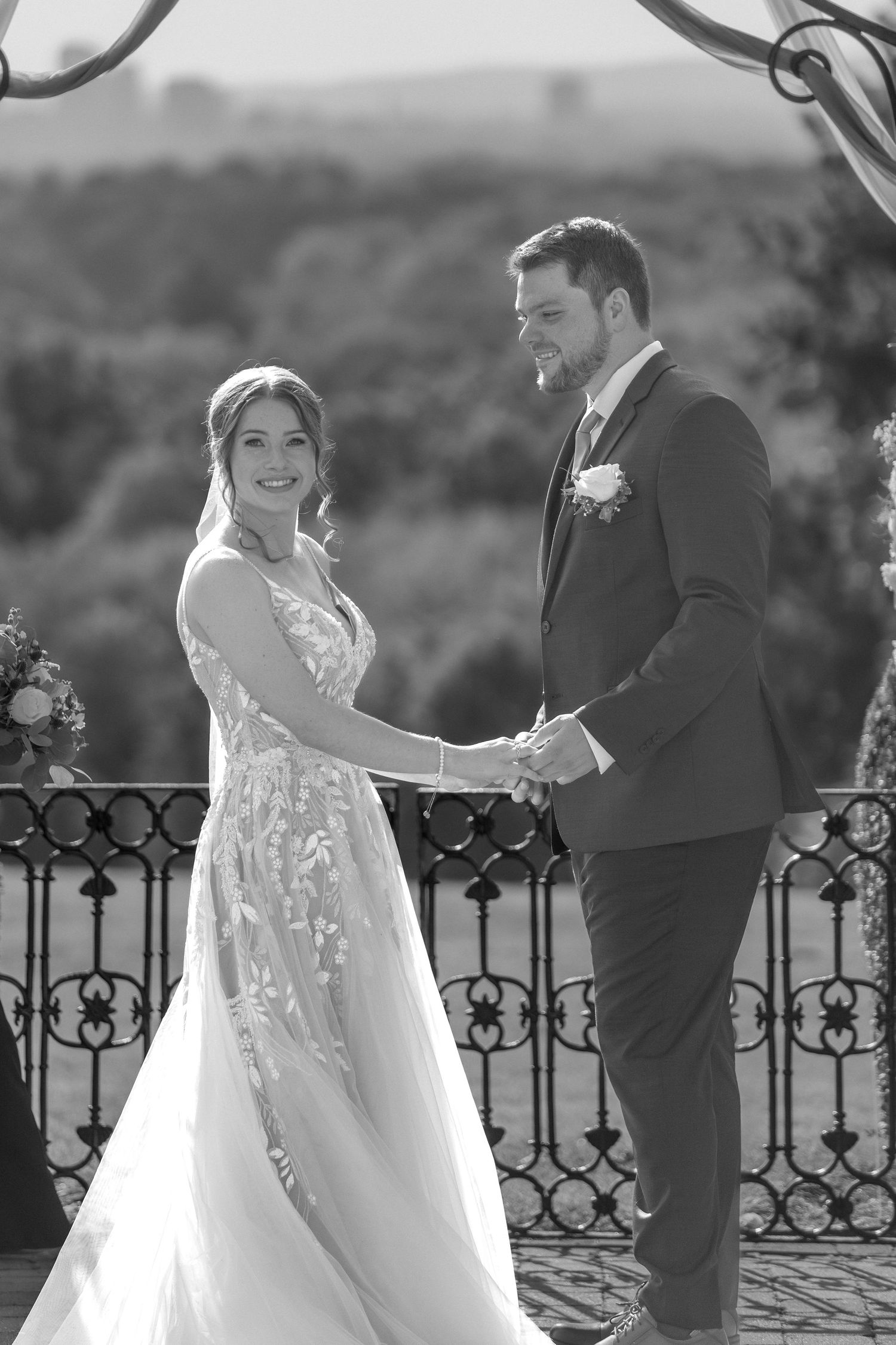Black and white portrait of newlyweds holding hands on an ornate balcony.