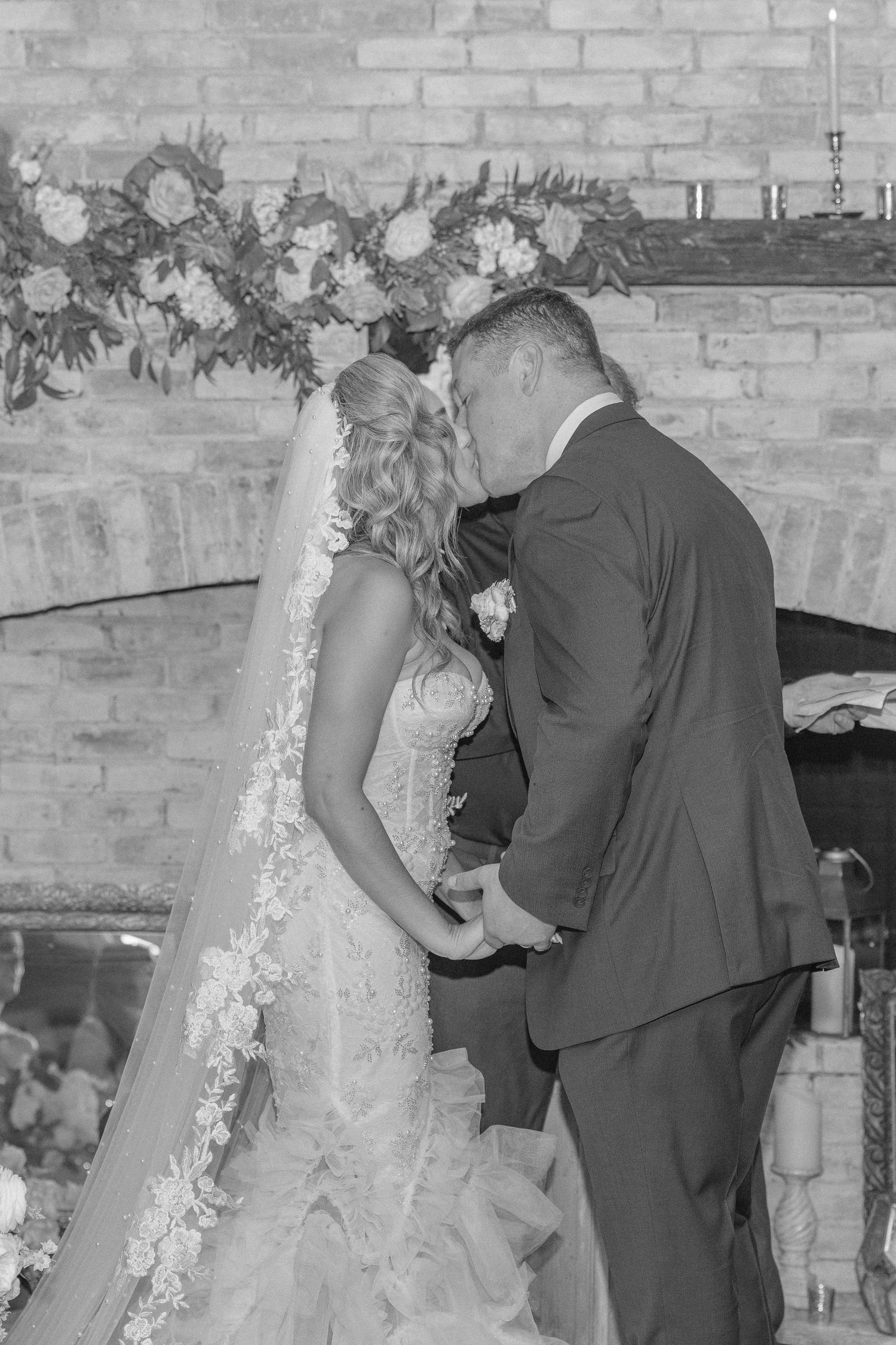 Romantic wedding ceremony moment in front of exposed brick wall with floral decorations.