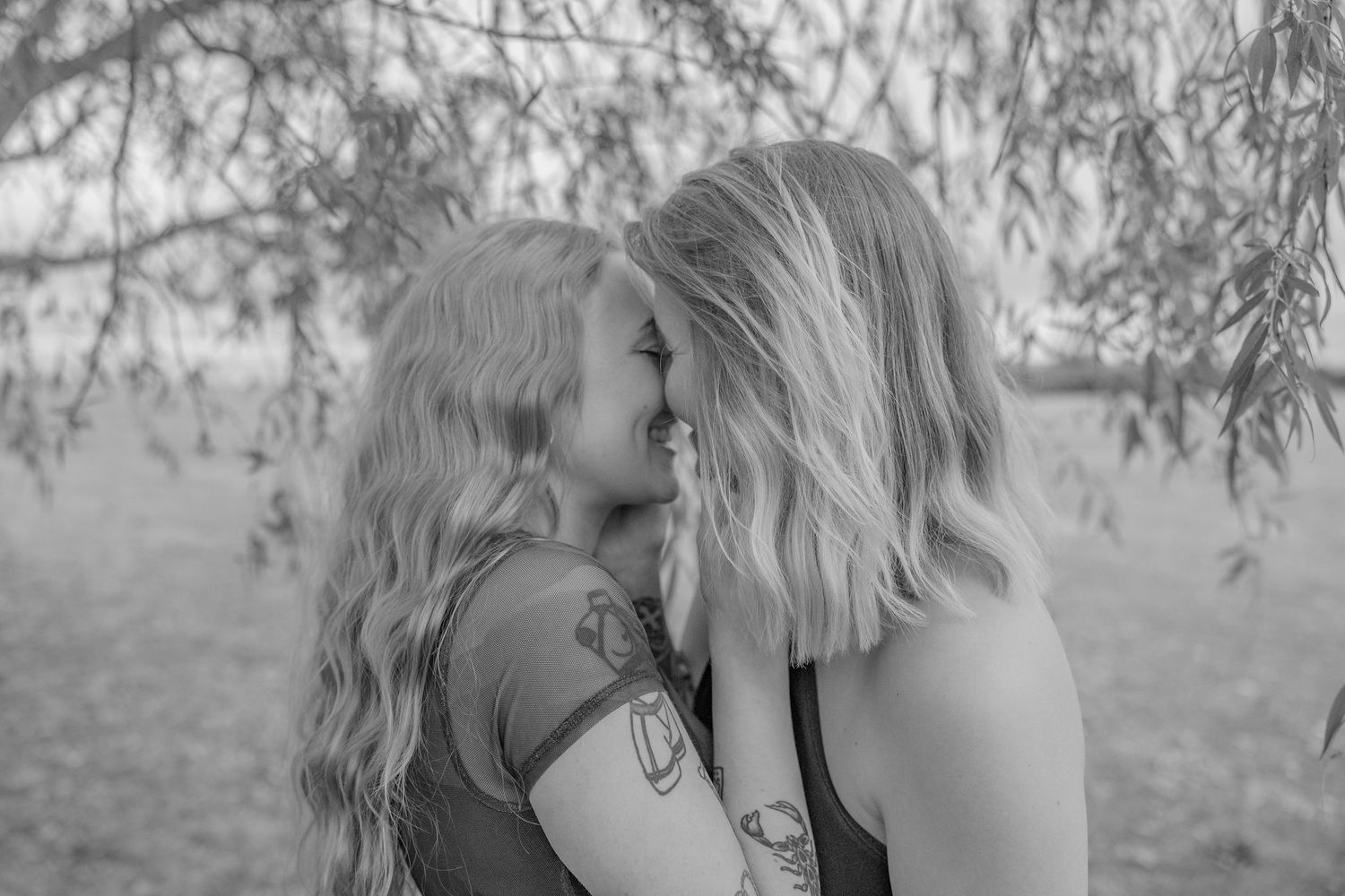 Two people sharing an intimate black and white moment under willow tree branches.