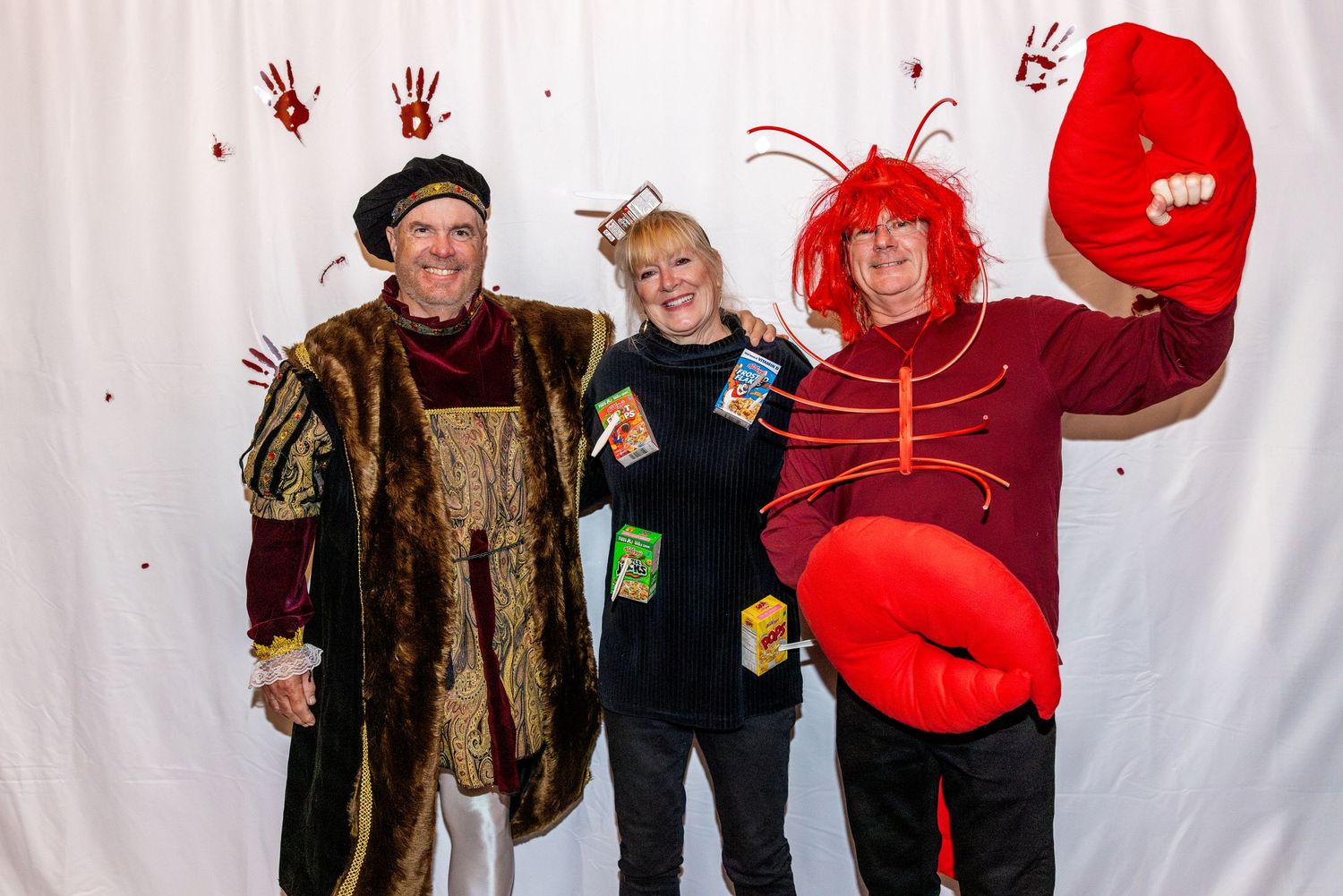 Three people in costume including a medieval noble and bright red lobster against white backdrop.