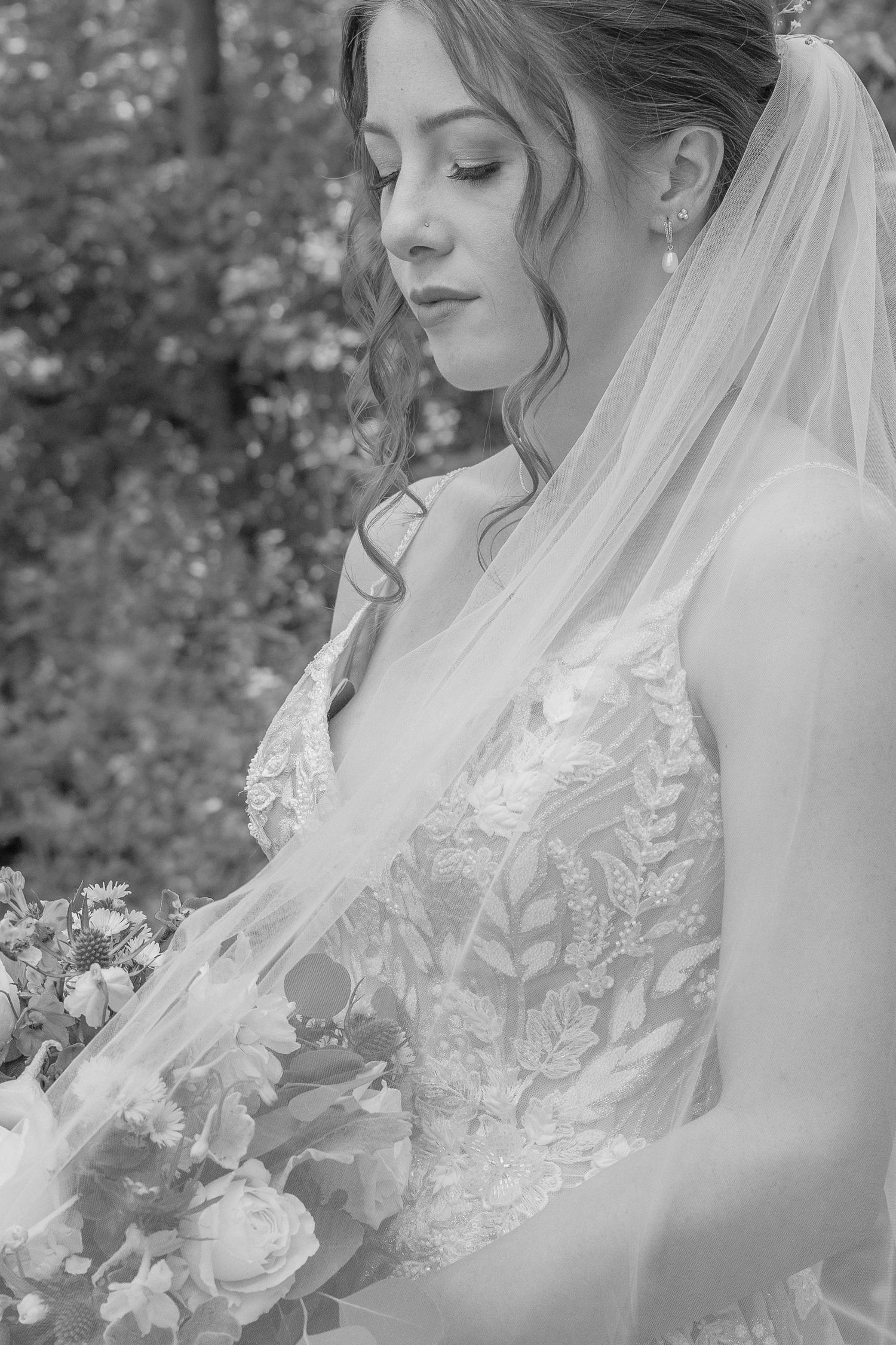 A romantic close-up shot of a bride in a lace wedding dress with veil holding a bouquet.