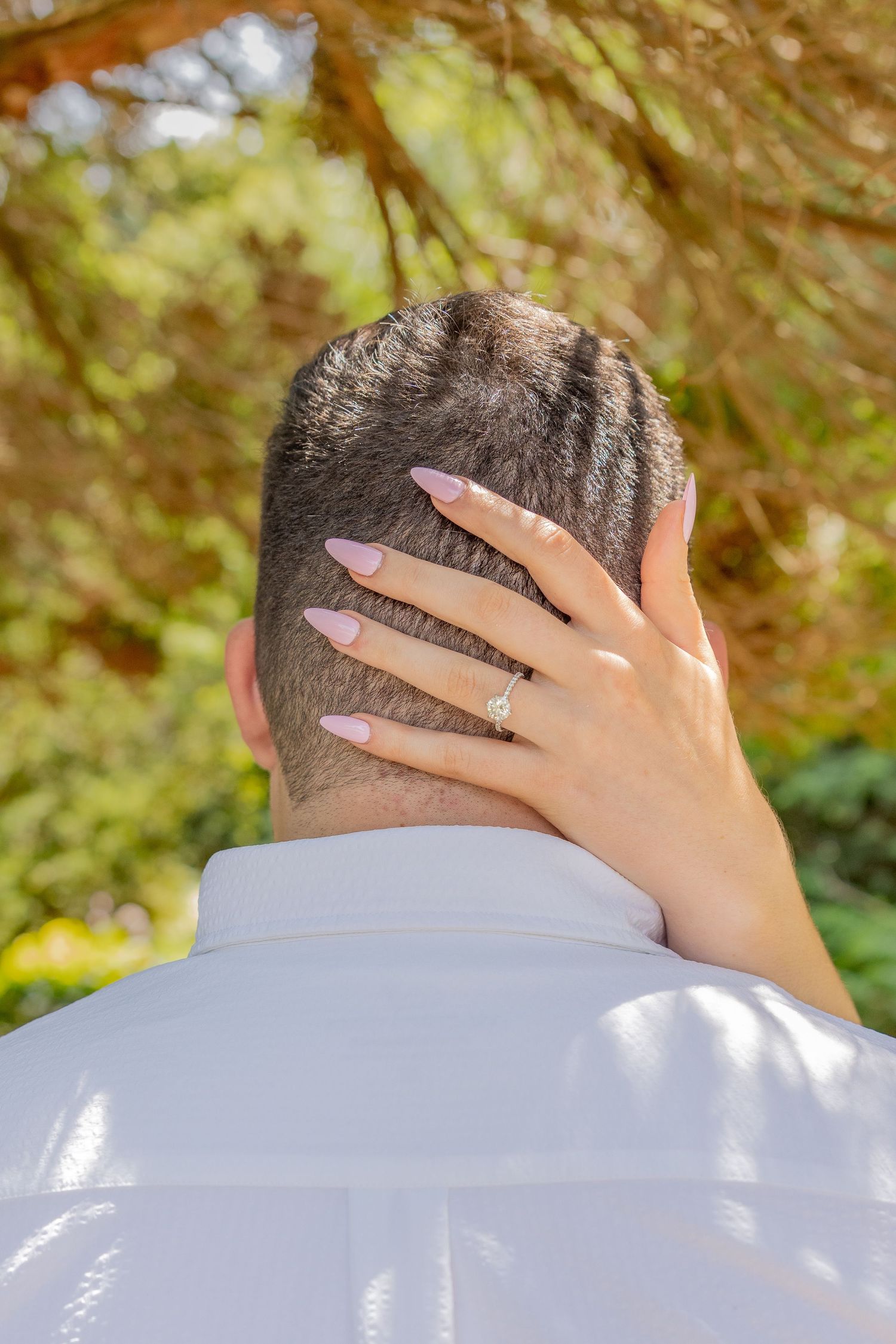 A close-up shot of a hand with manicured nails resting on the back of someone wearing a white shirt.