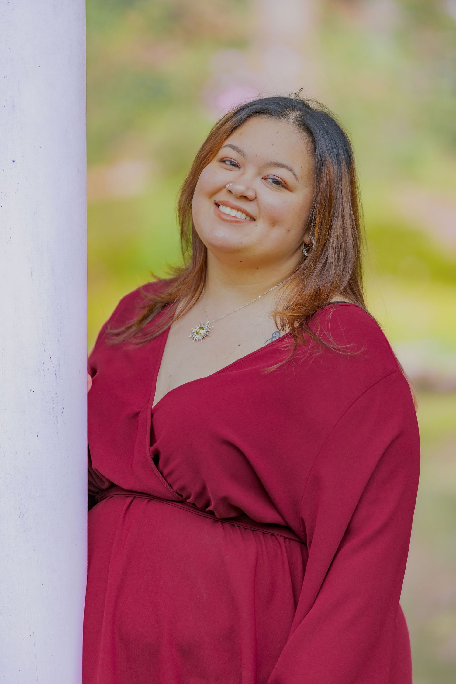 Portrait of person in burgundy wrap dress smiling against blurred garden background.