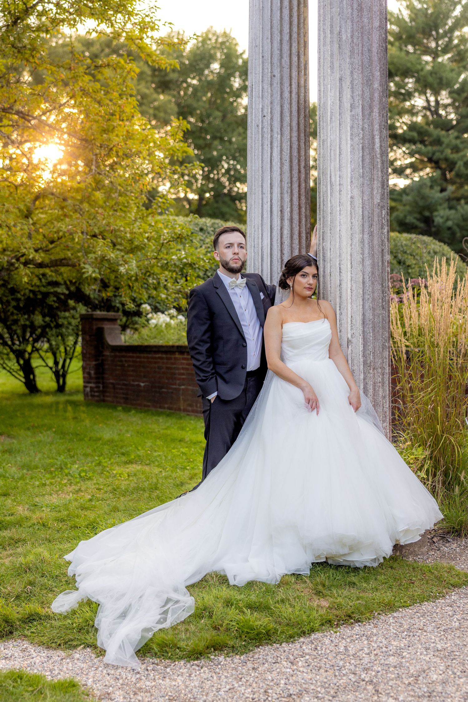Couple poses against marble columns during golden hour wedding photoshoot.