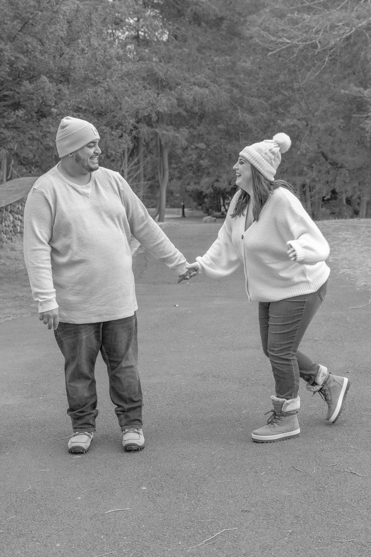 Black and white photo of a couple in winter wear sharing a playful dance moment outdoors.