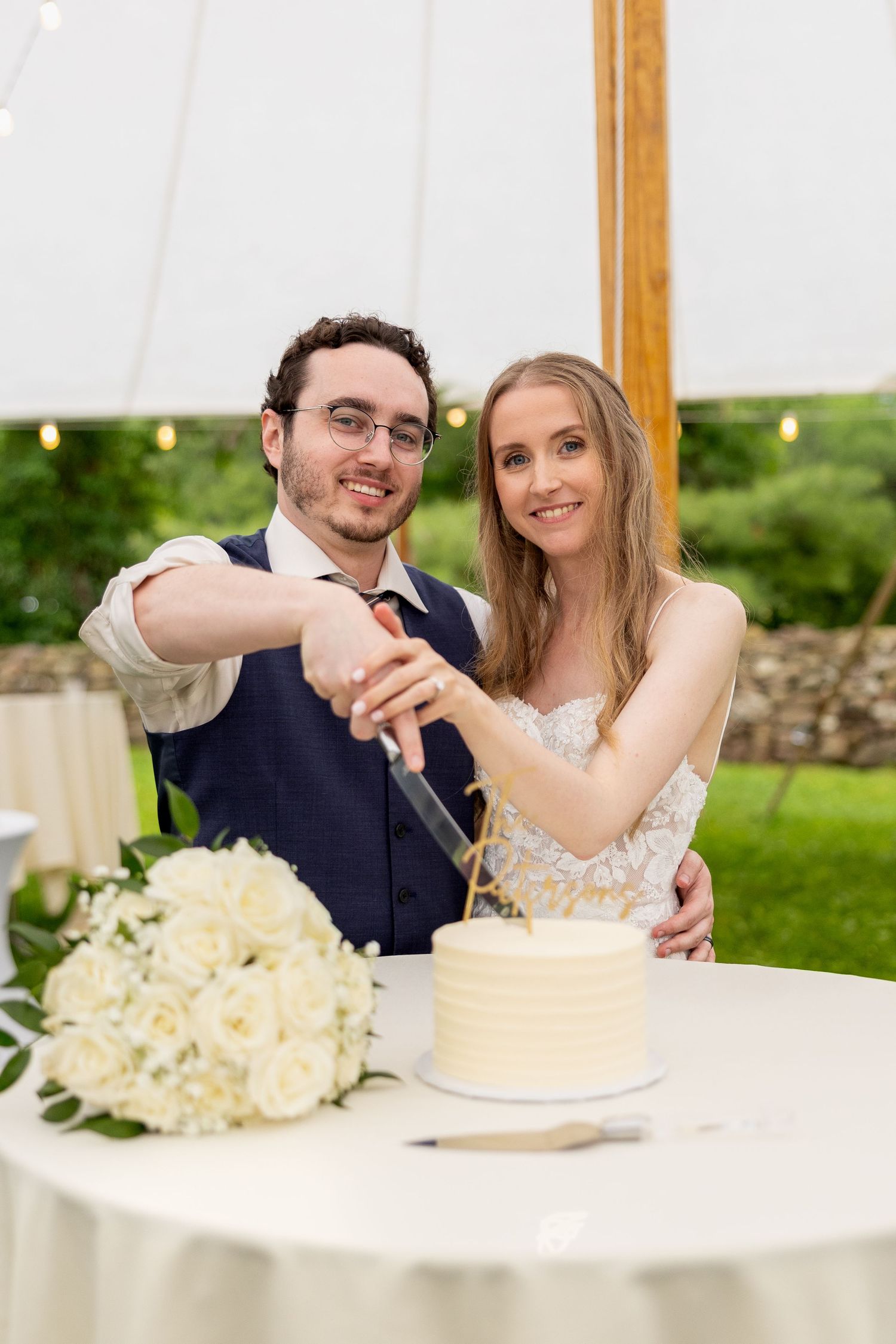 A pair cuts their delicate white wedding cake together at an elegant reception with floral decorations on the table.