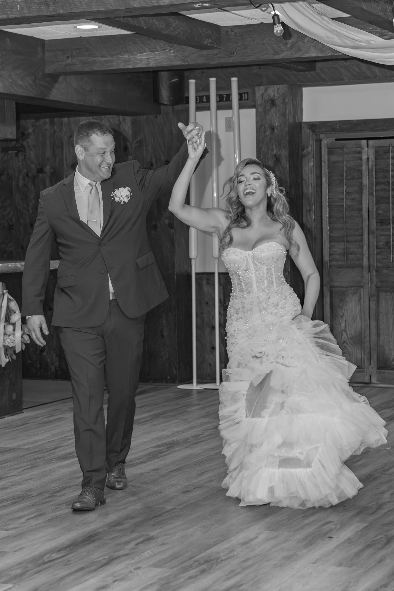 A couple shares a playful moment during their first dance at a rustic wedding reception venue with wooden beams.