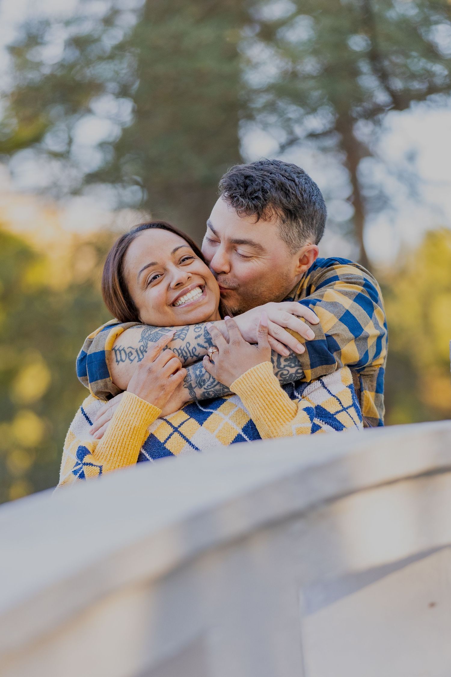 A couple wearing coordinated plaid and yellow outfits share an affectionate moment outdoors.